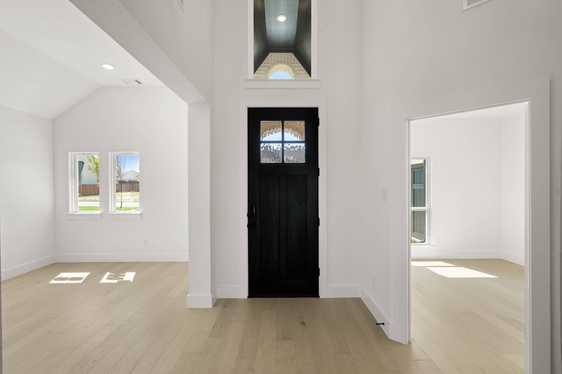Spacious entryway with black door, high ceiling, and light wood flooring.