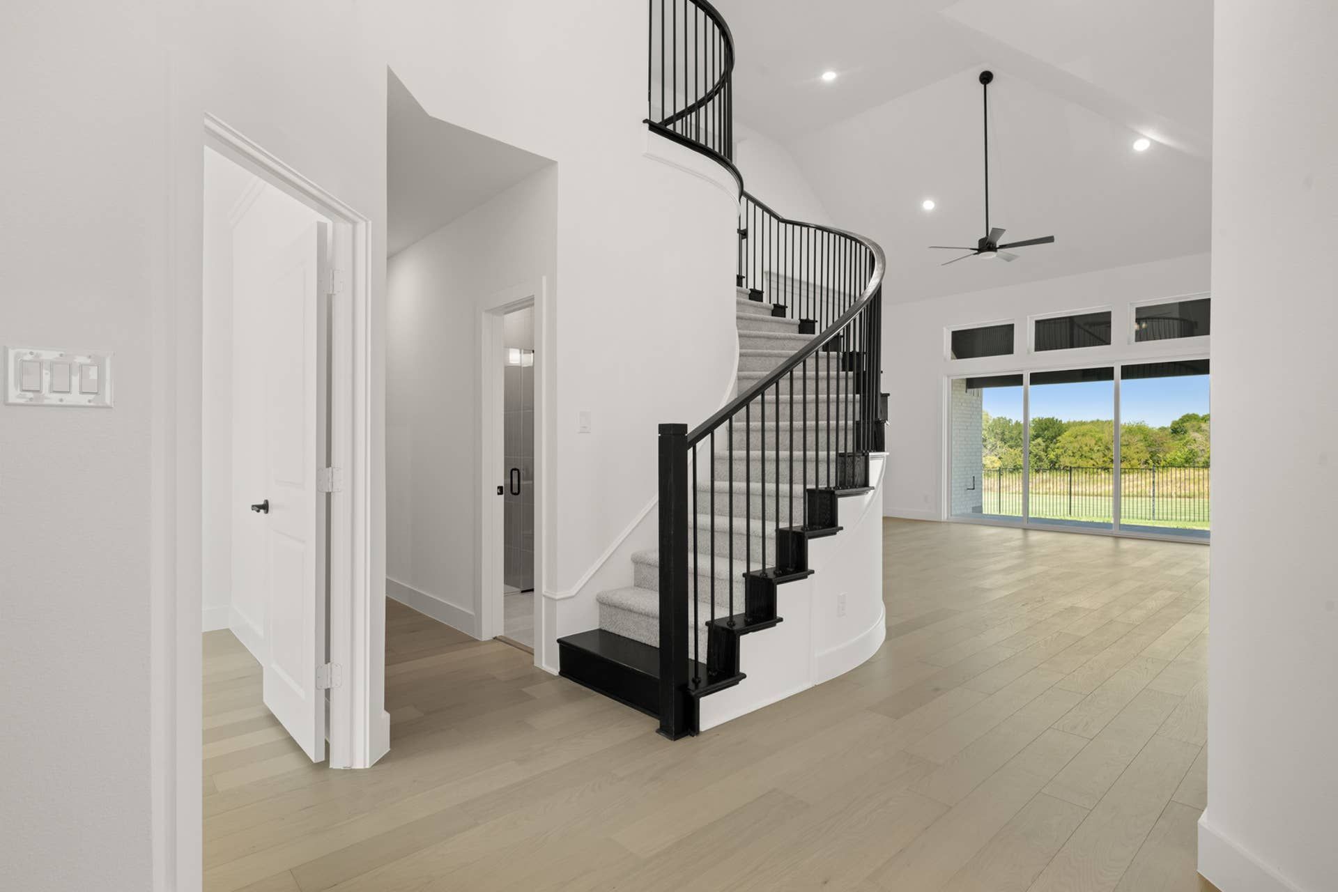 Elegant entryway with curved staircase, high ceilings, and expansive windows overlooking greenery.