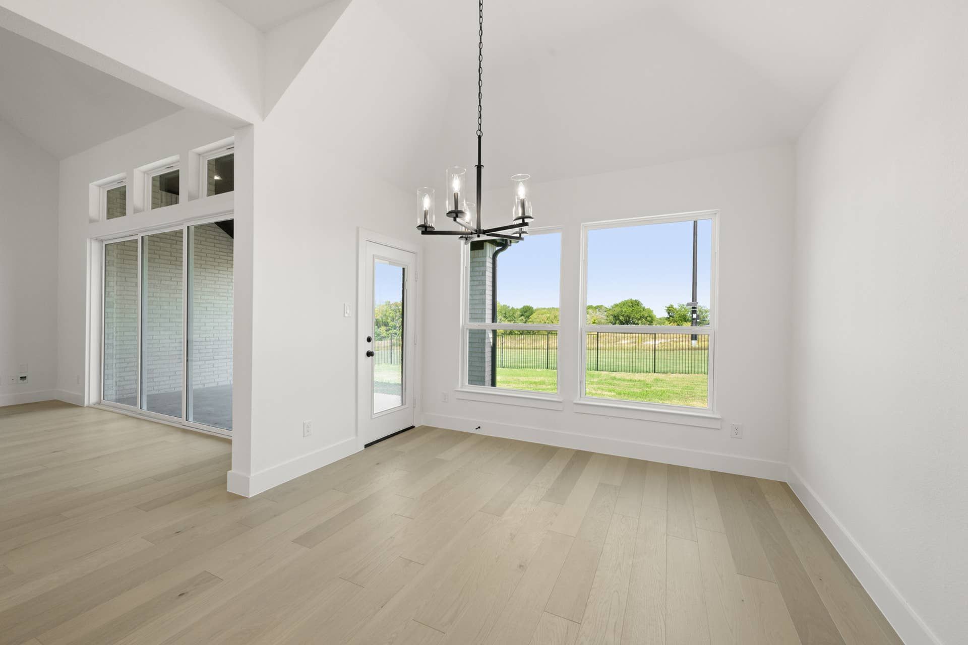 Bright dining area with modern chandelier and large windows overlooking a lawn.