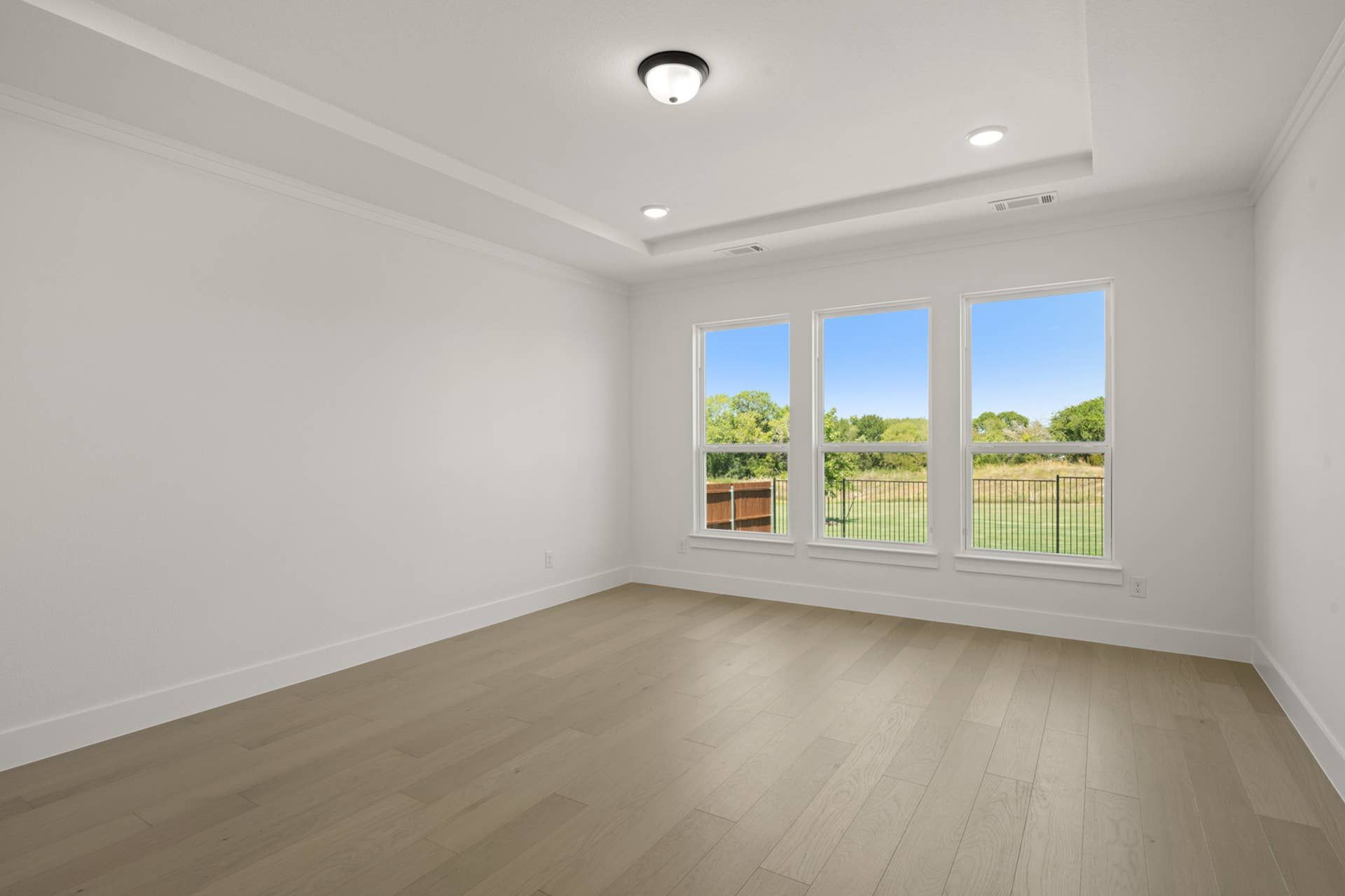 Spacious primary suite with large windows and tray ceiling, overlooking backyard.