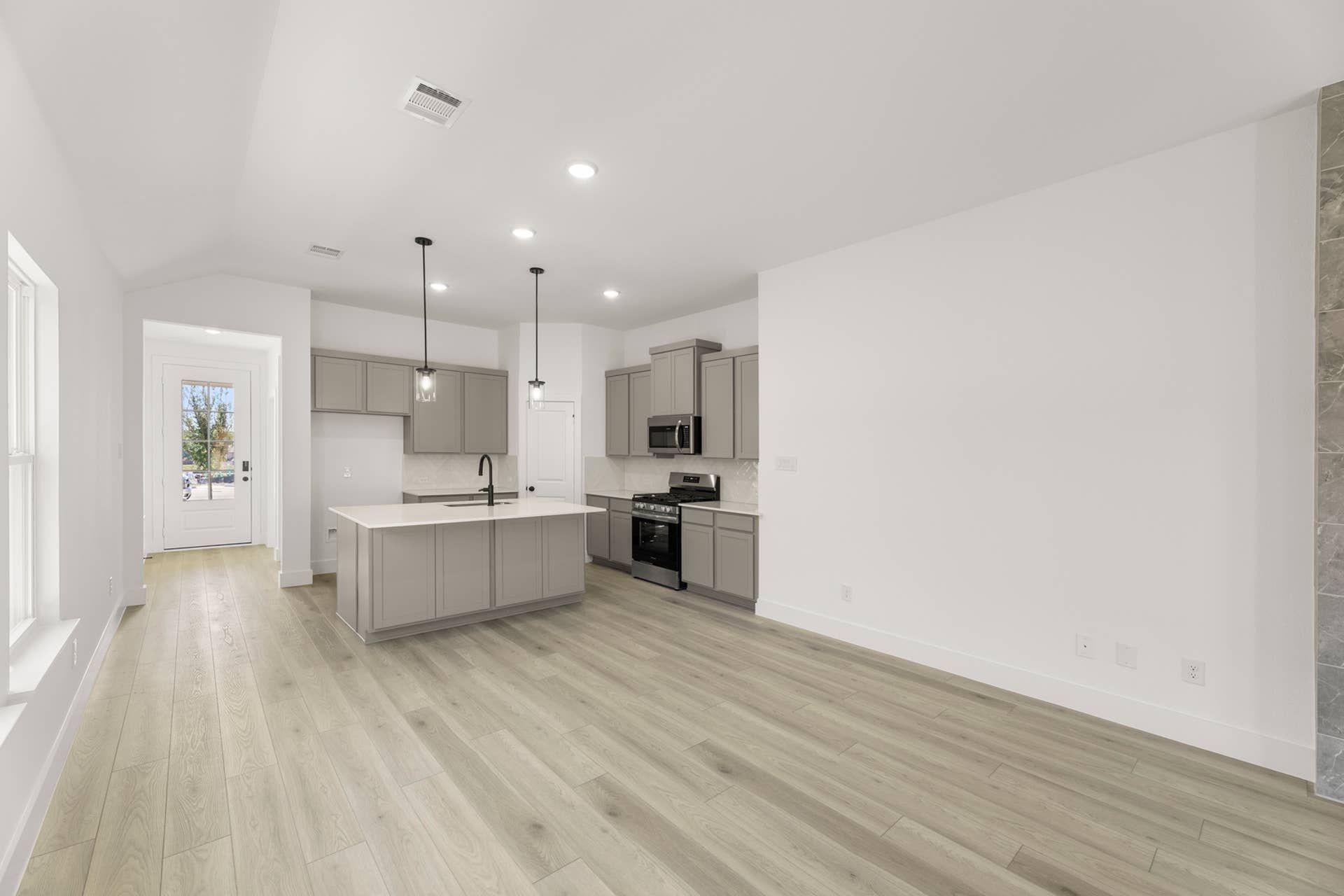 Modern kitchen with gray cabinets, island, and pendant lighting in open floor plan.