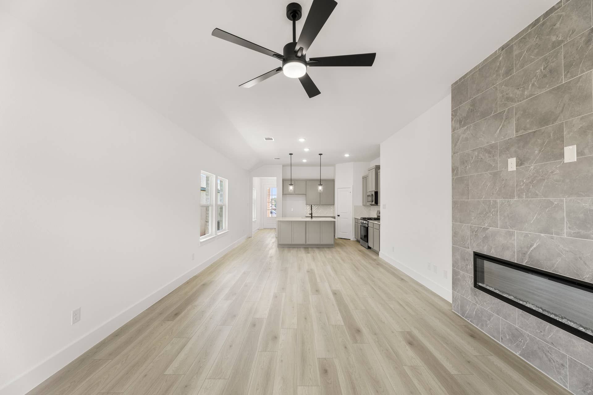 Spacious modern family room with ceiling fan, hardwood floors, and stone accent wall fireplace.