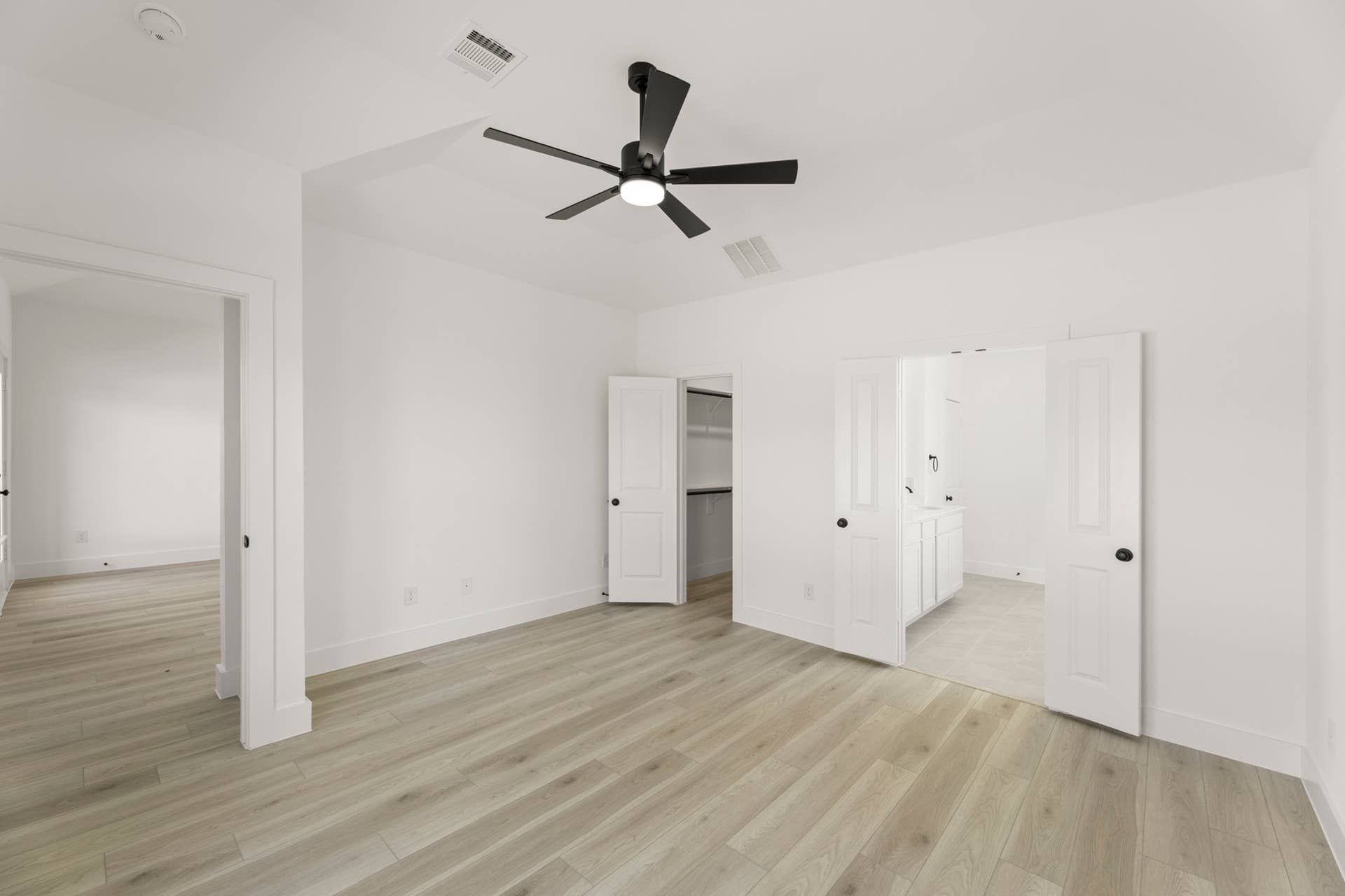 Spacious bedroom with light wood flooring, ceiling fan, and walk-in closet access.