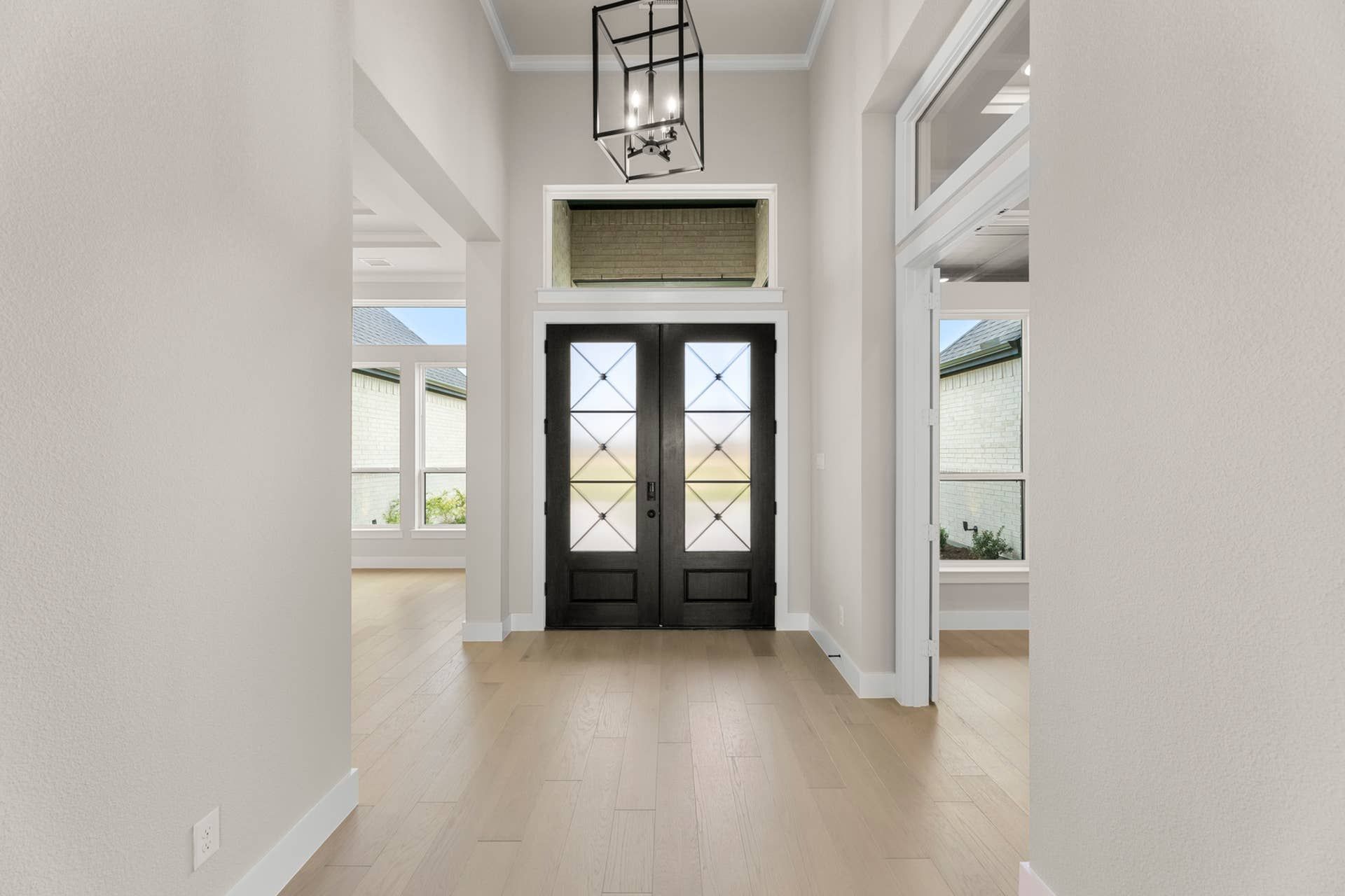 Spacious entryway with double doors and modern chandelier lighting.
