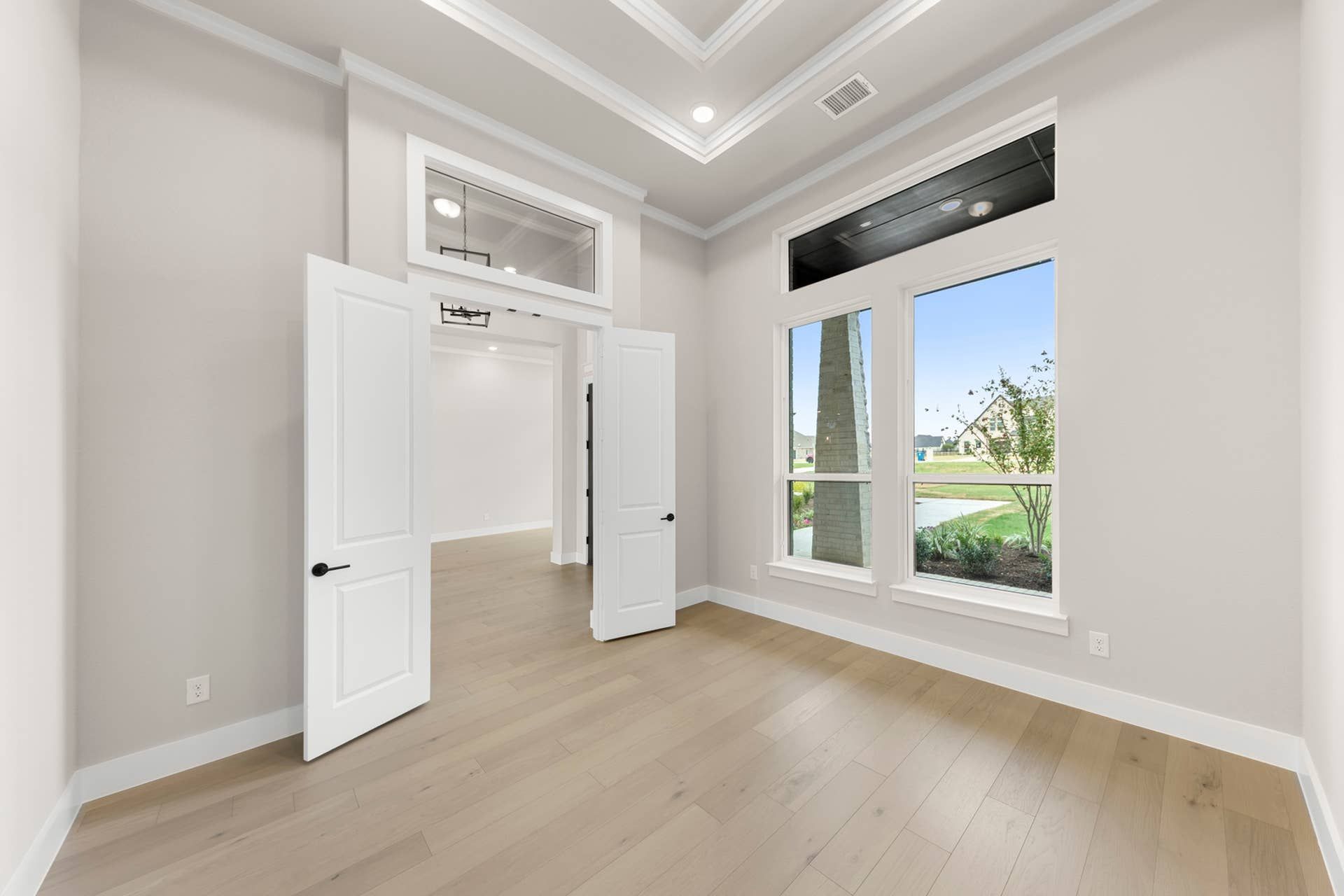 Spacious study with double doors, large windows, and tray ceiling.