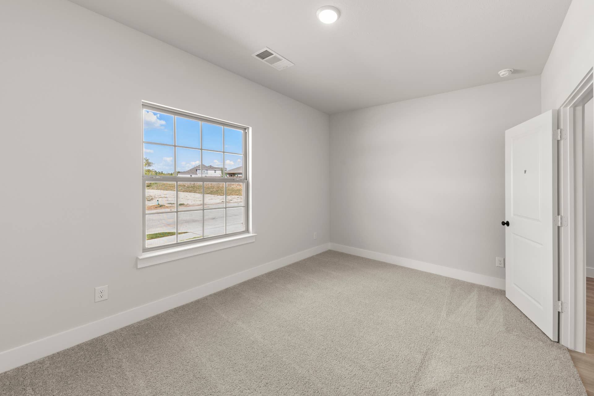 Bright, carpeted bedroom with large window and neutral walls.