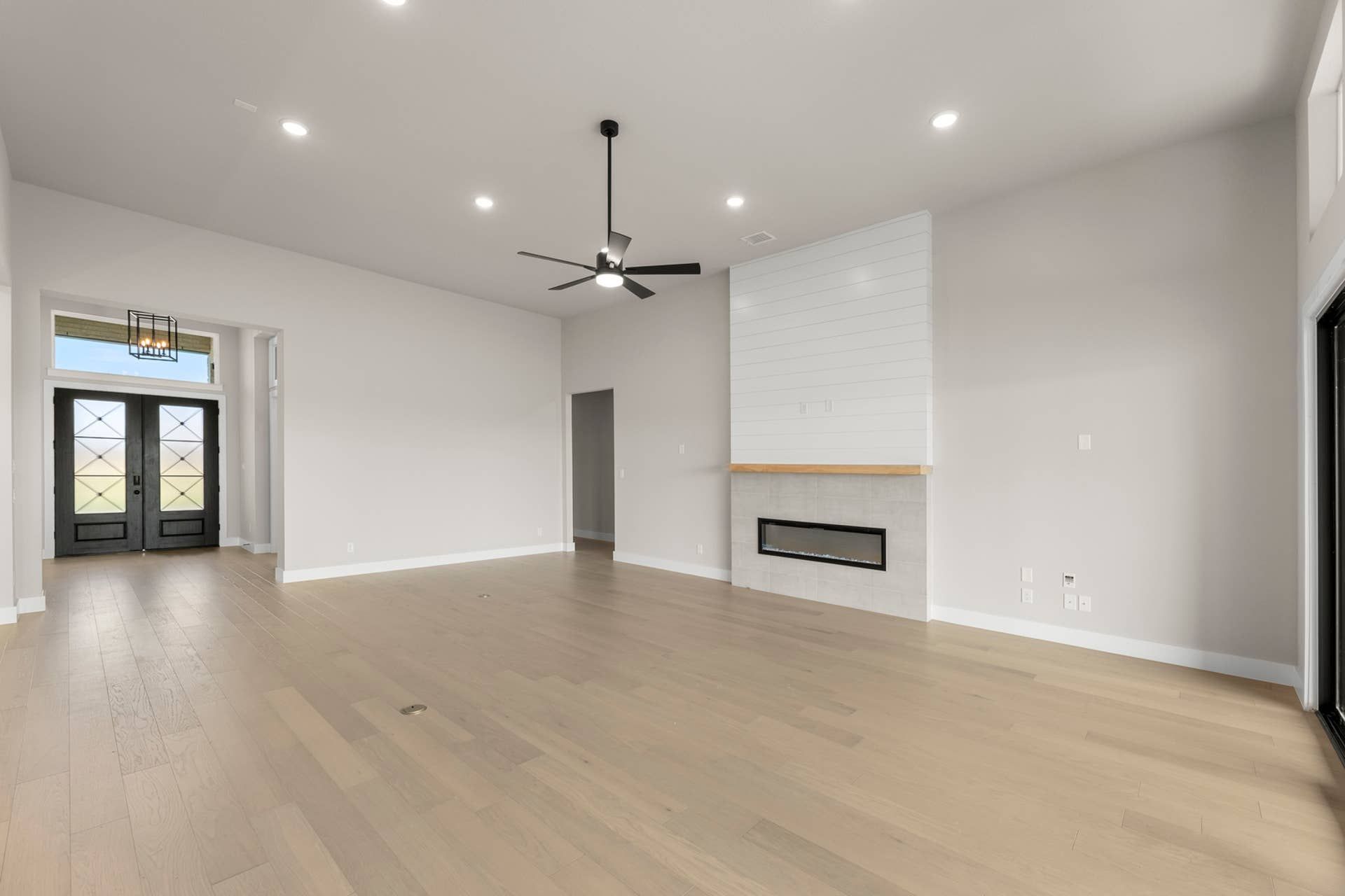 Spacious living room with hardwood floors, modern fireplace, and large front doors.