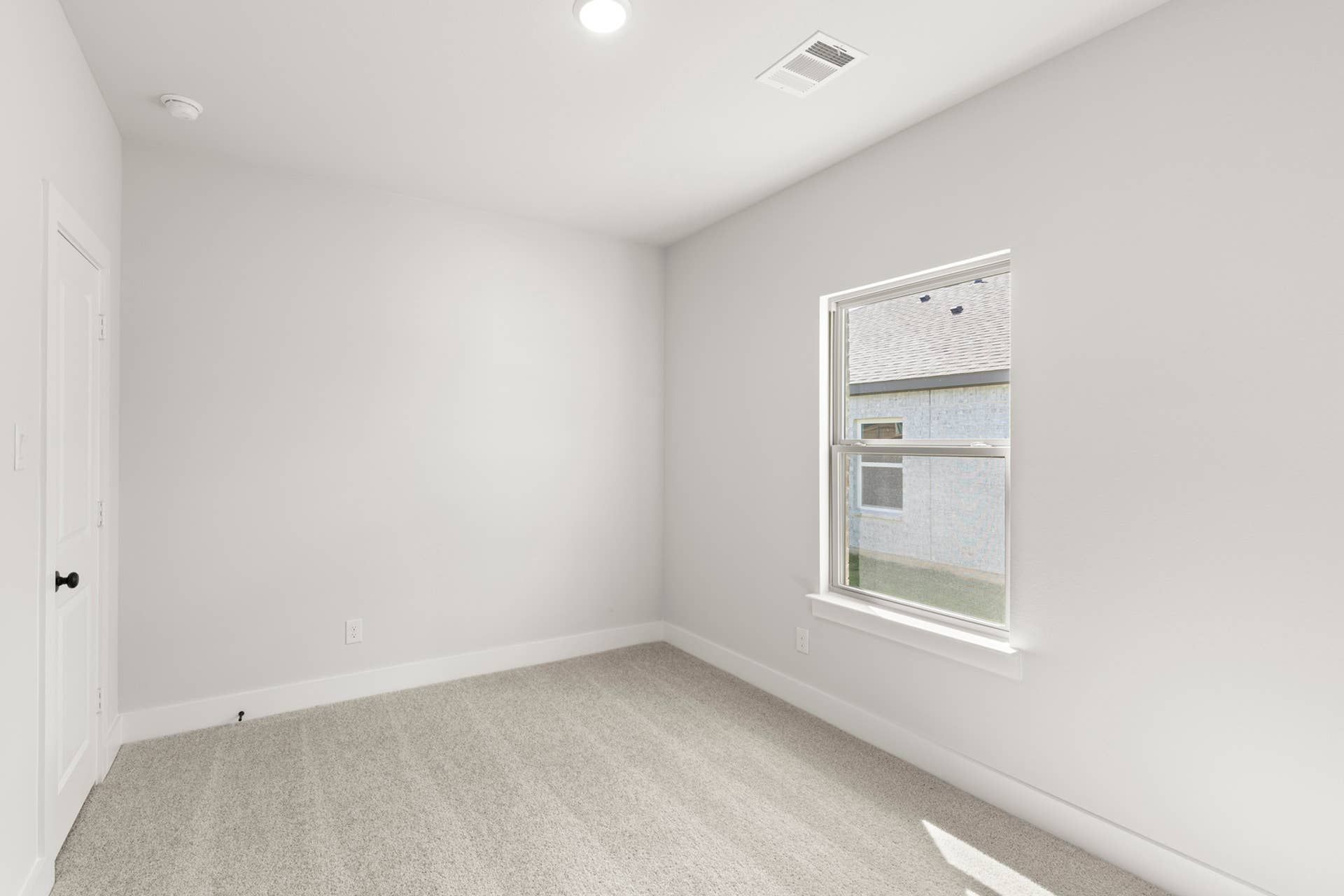 Bright, minimalist bedroom with neutral walls and carpet, featuring a large window.