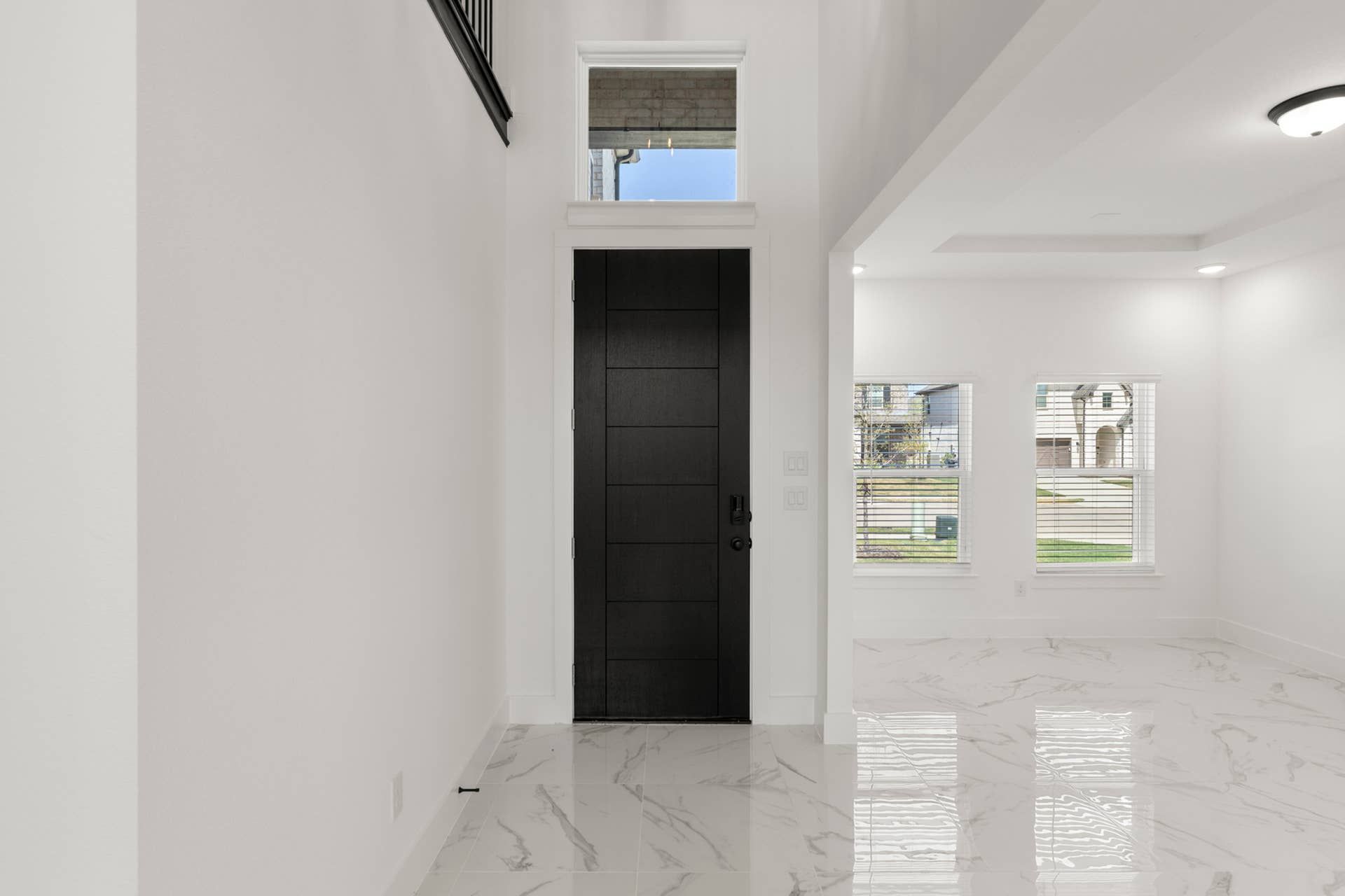 Spacious entryway with sleek black door and marble flooring.