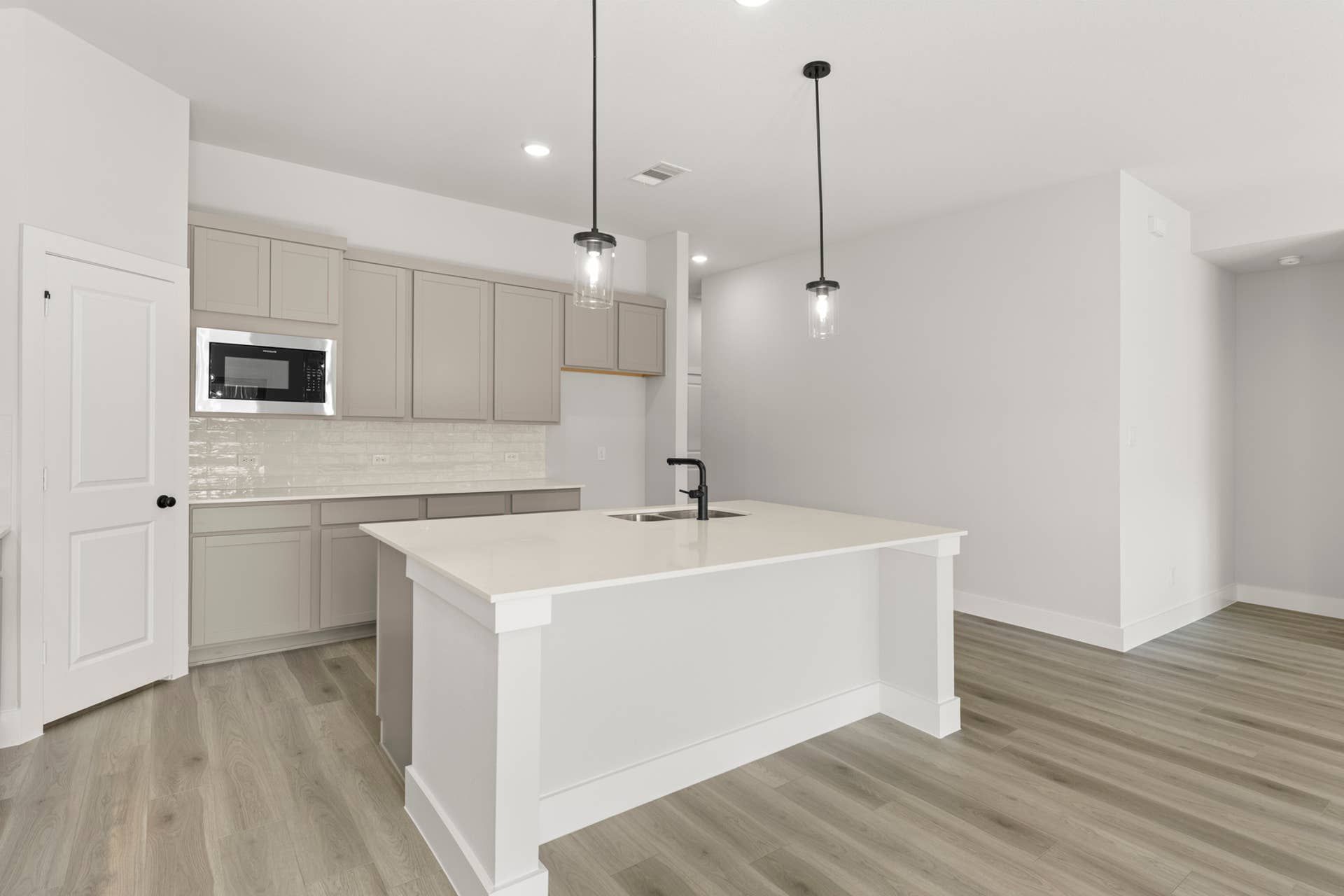 Modern kitchen with white island, pendant lights, and beige cabinetry.