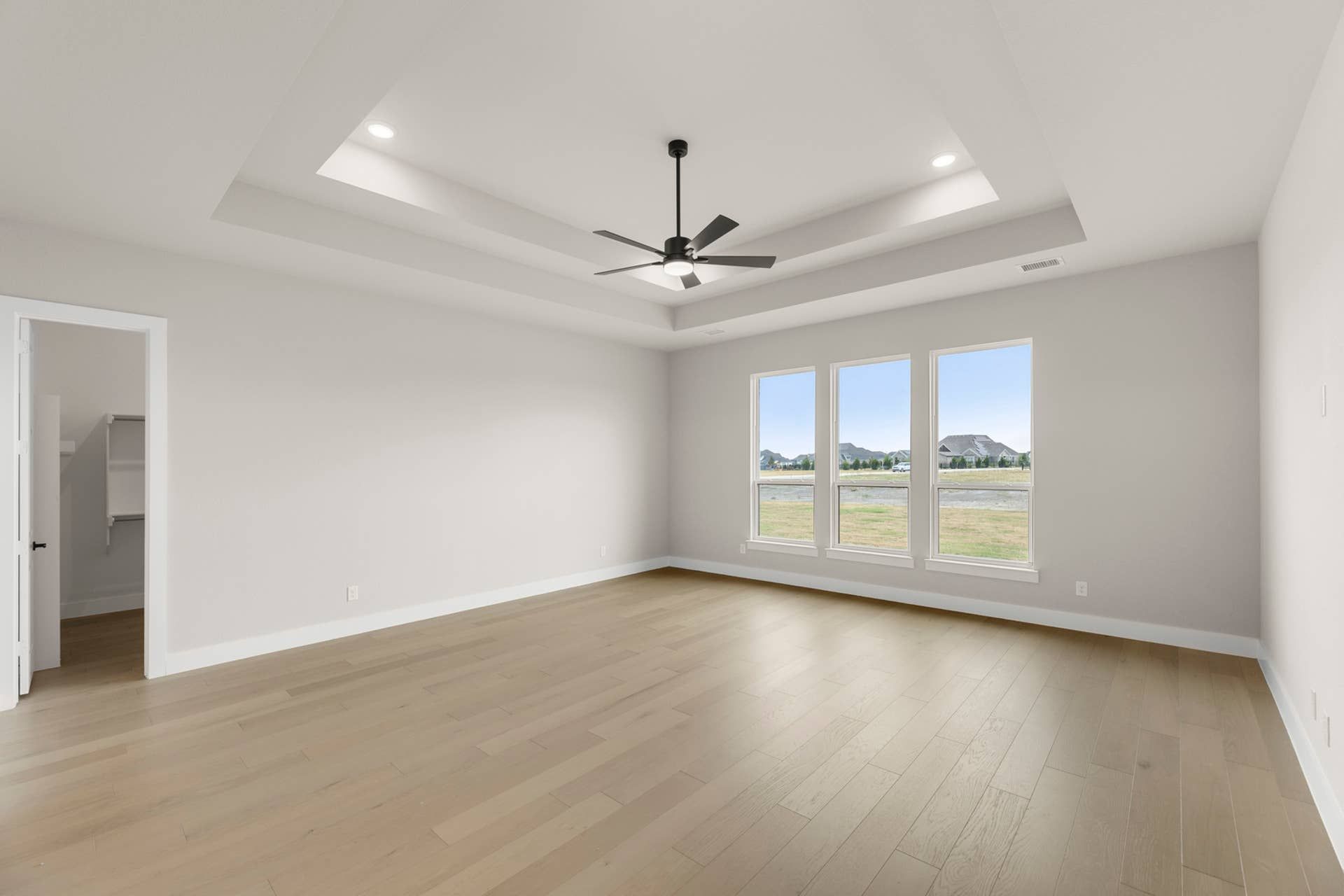 Spacious interior with tray ceiling, modern fan, and large windows overlooking landscape.