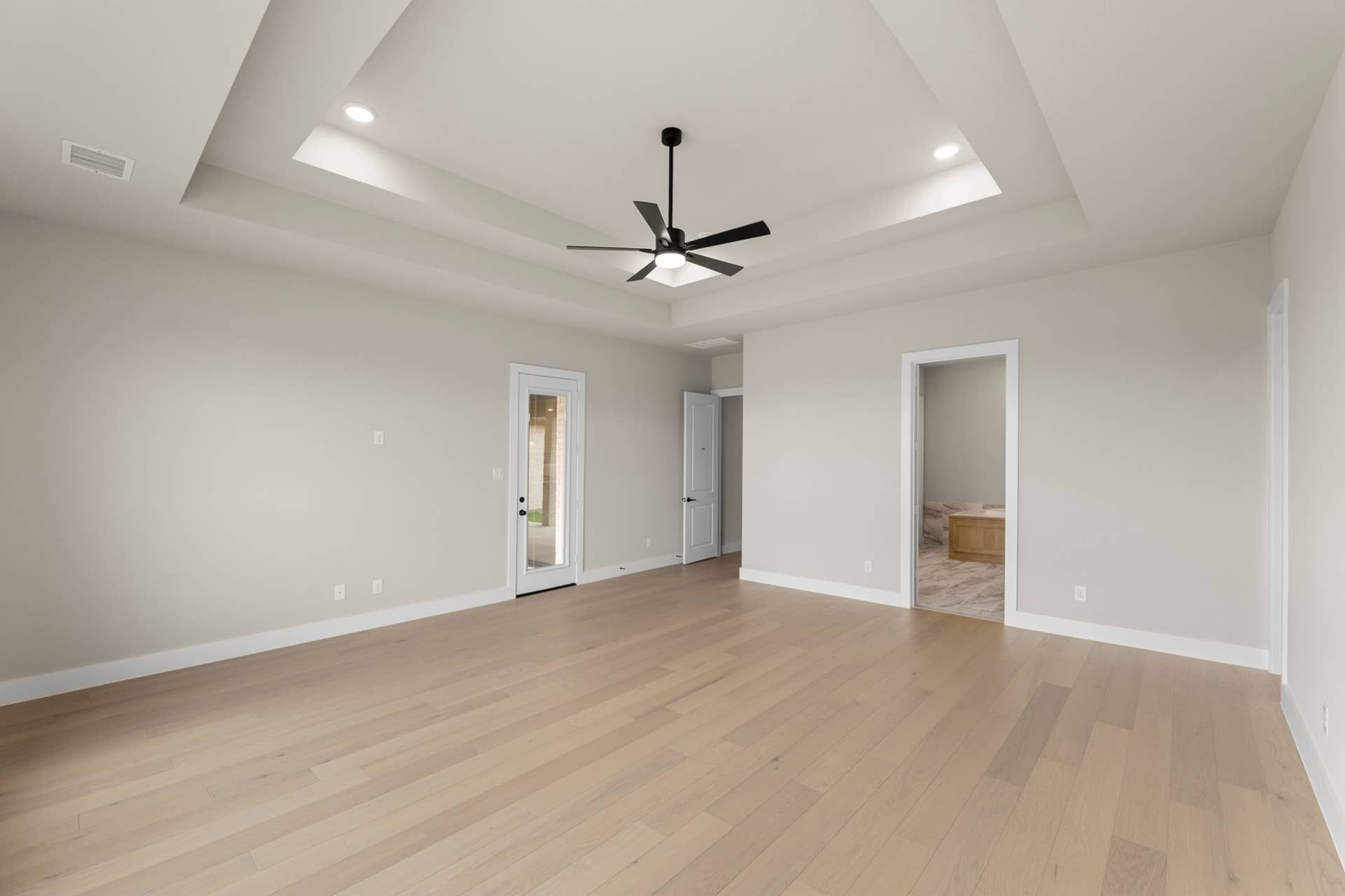 Spacious interior with light wood floors and tray ceiling featuring recessed lighting.