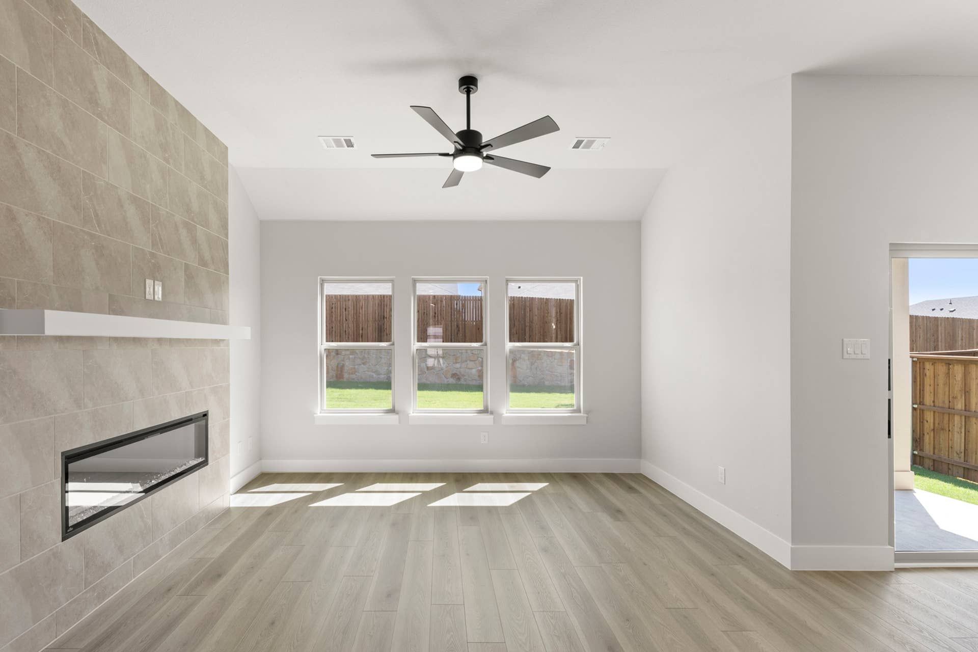 Spacious living room with modern fireplace, ceiling fan, and large windows.