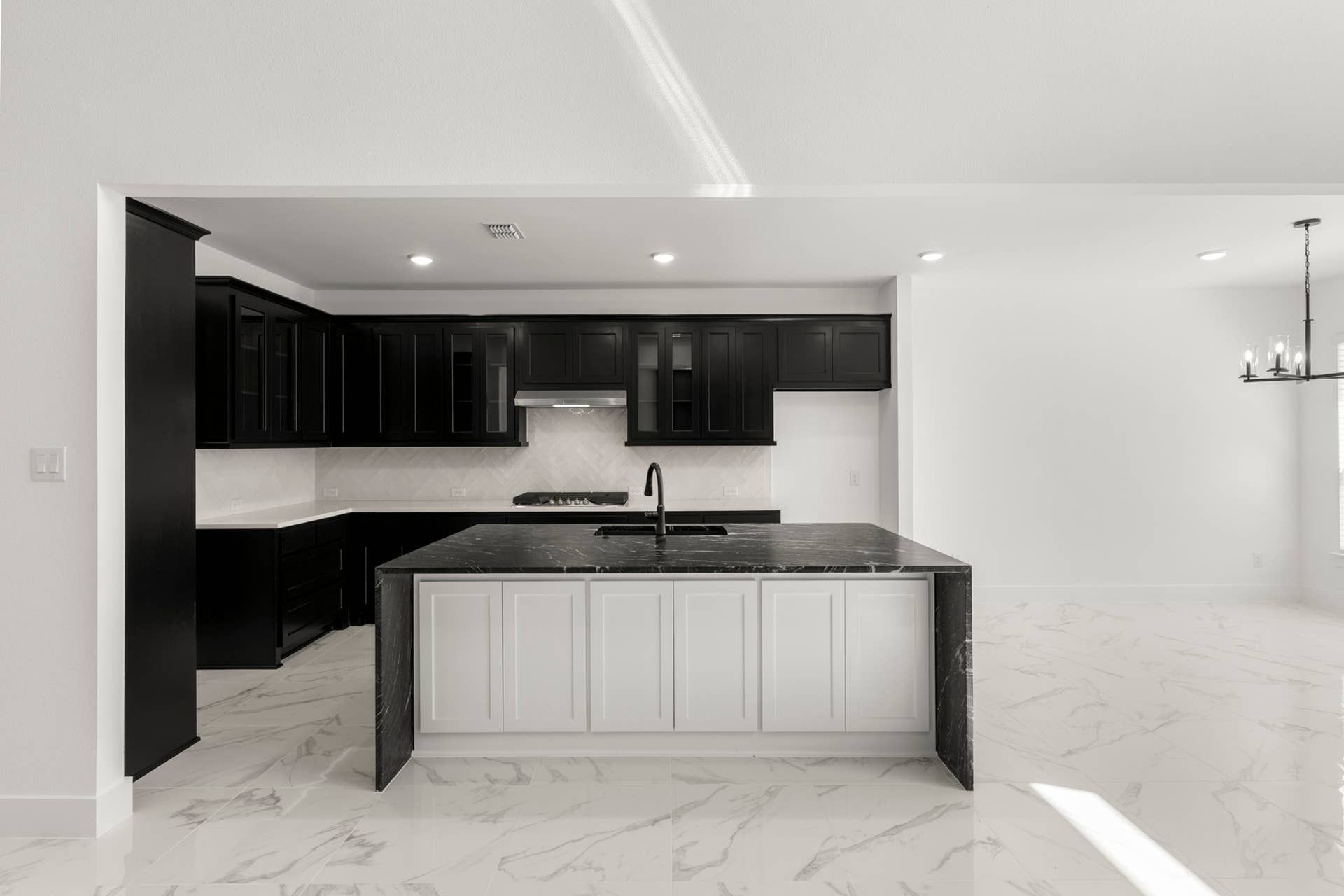 Modern kitchen with black cabinets, marble countertops, and elegant lighting.