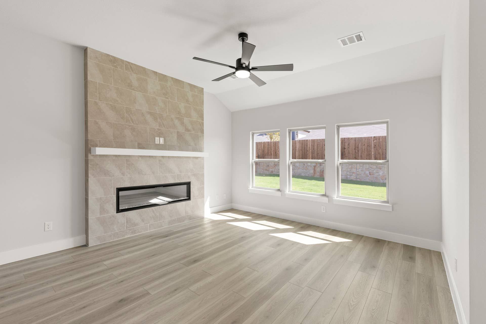 Spacious living room with modern fireplace, large windows, and ceiling fan.