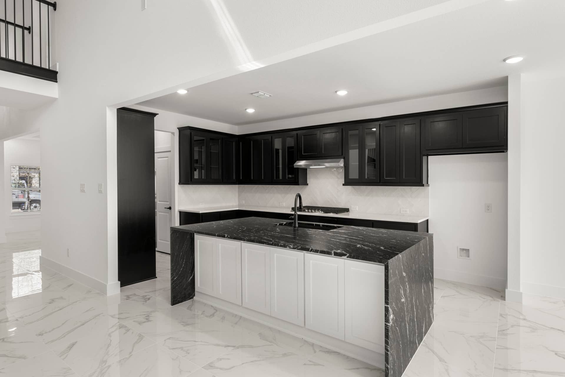 Modern kitchen with black cabinetry, marble countertops, and high ceilings.