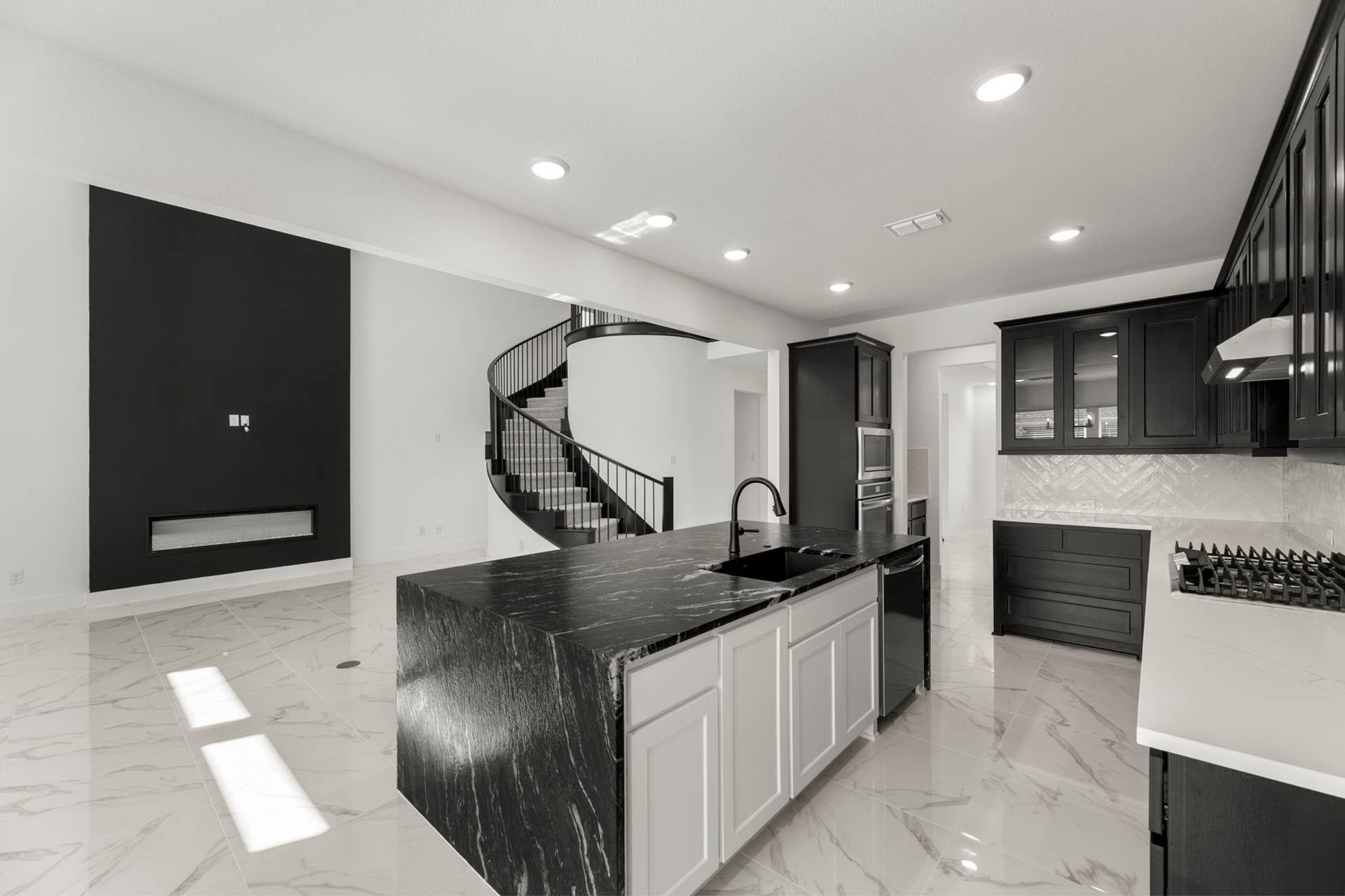 Sleek modern kitchen with black and white cabinetry, island, and spiral staircase.