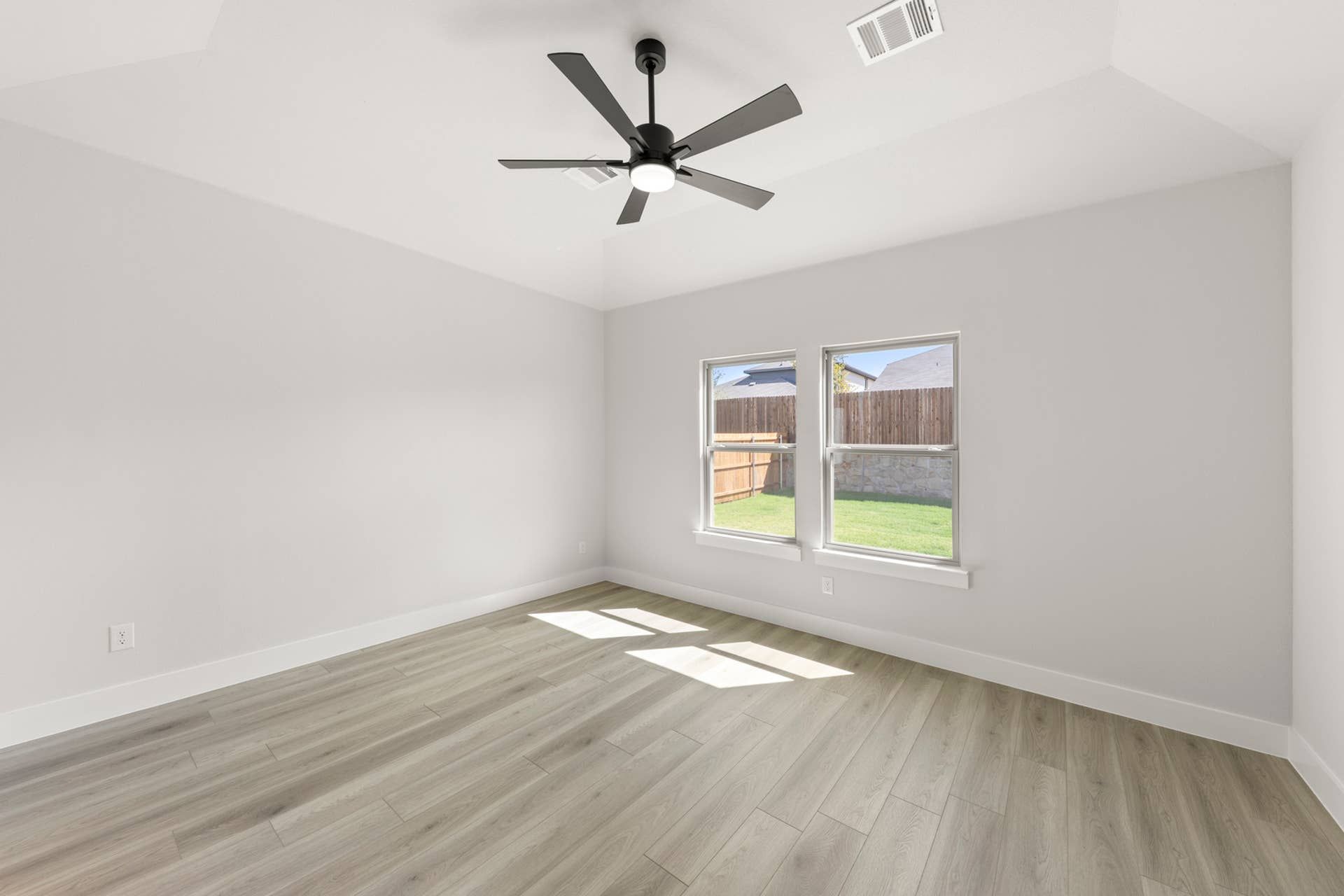 Bright bedroom with wood flooring, large windows, and ceiling fan.