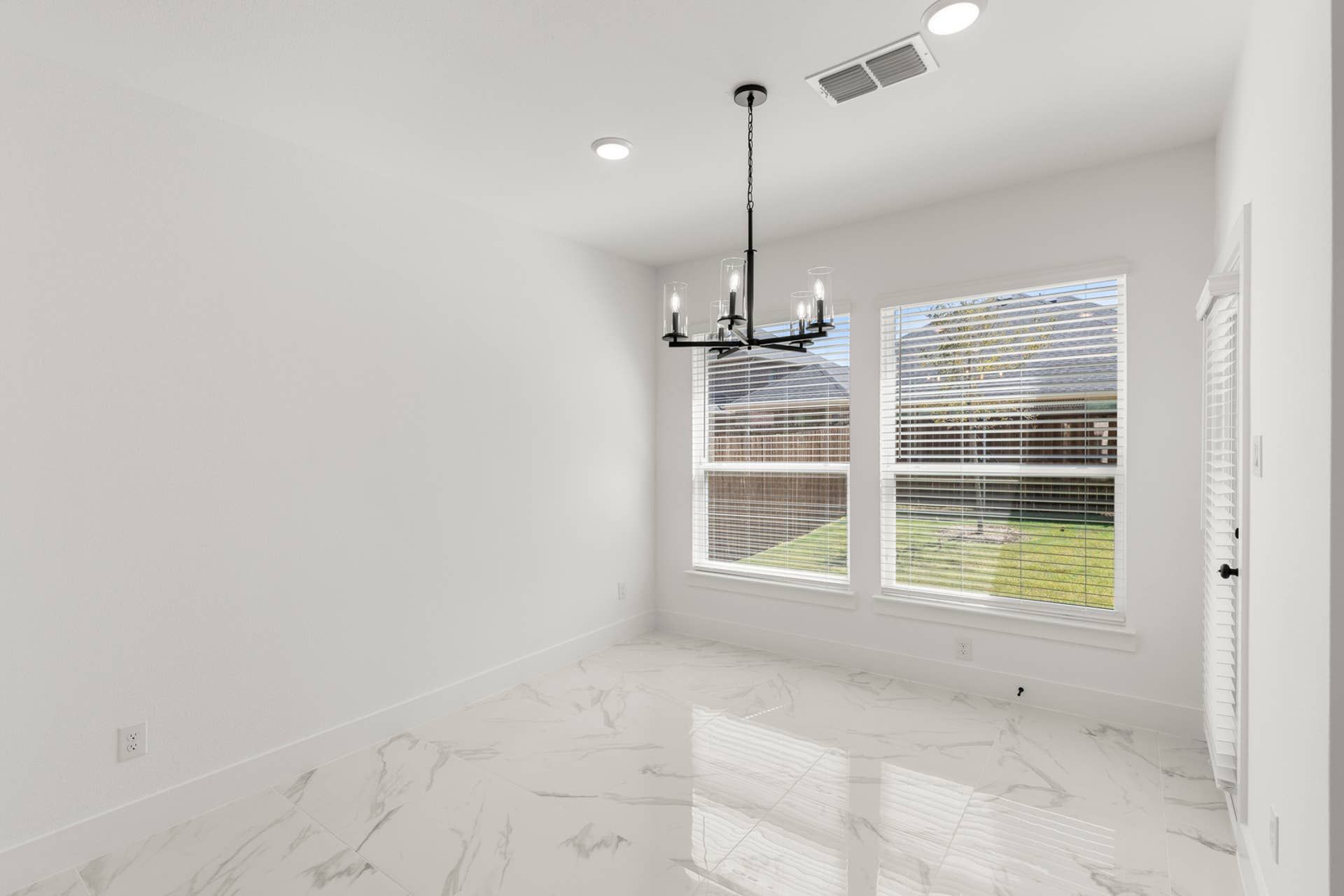Bright dining nook with chandelier and marble tile flooring overlooking backyard.