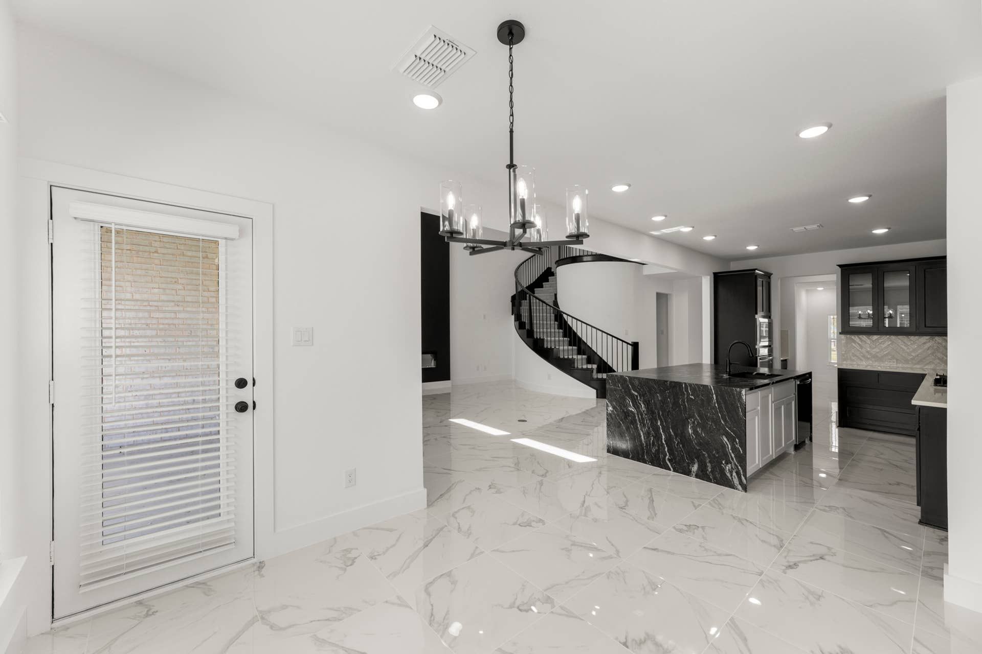 Modern kitchen with marble island, spiral staircase, and elegant chandelier lighting.