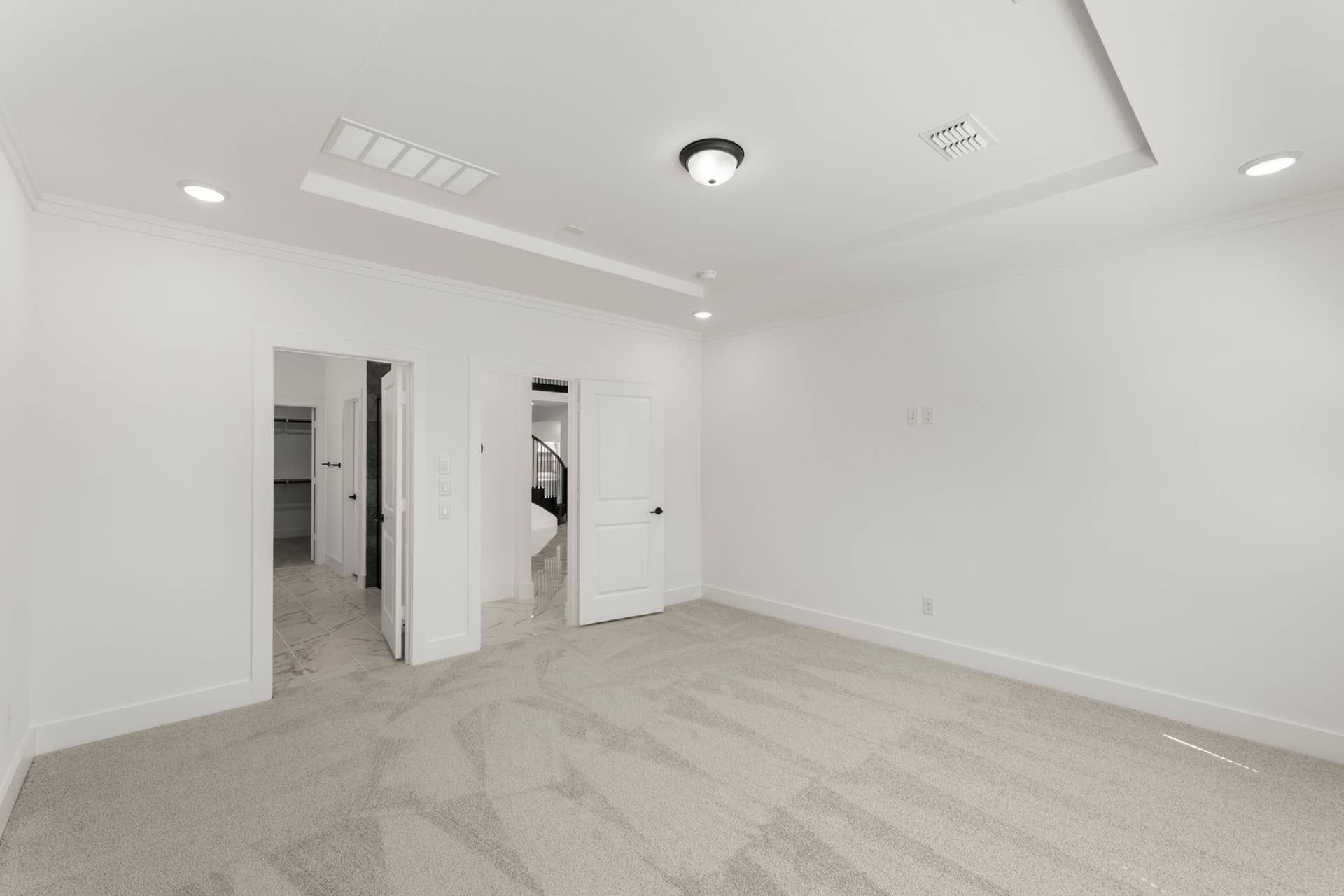 Spacious, carpeted bedroom with recessed lighting and white walls.