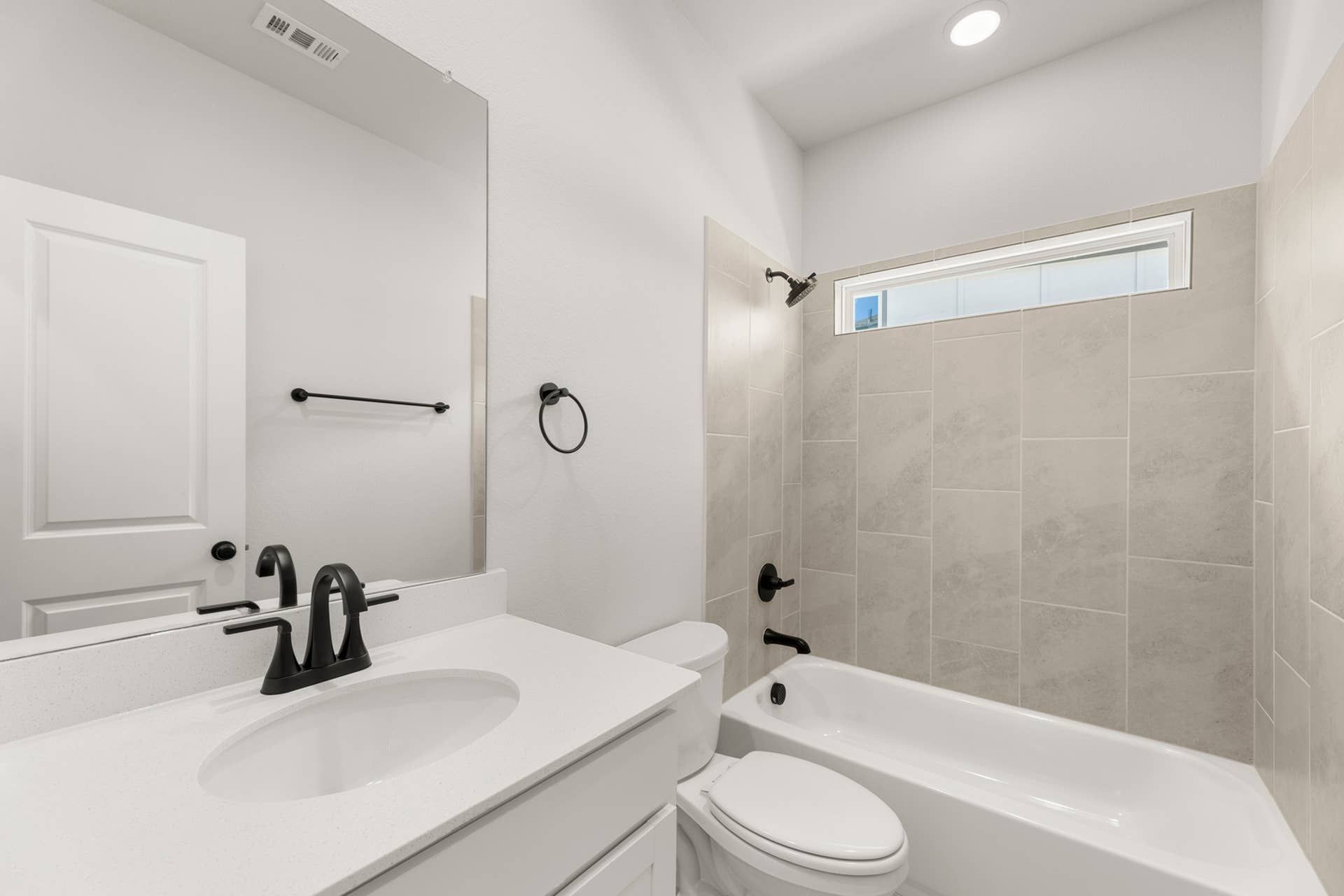 Modern bathroom with sleek fixtures, white countertop, and tiled bathtub area.