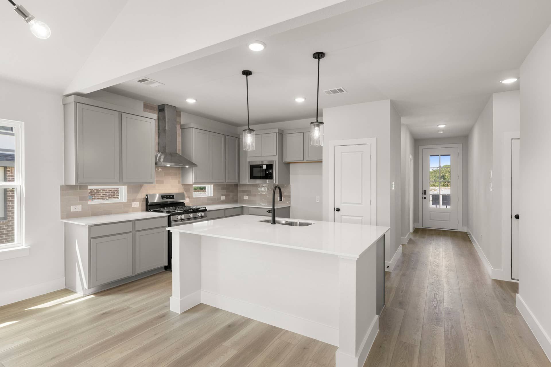 Modern kitchen with gray cabinets, island, pendant lights, and stainless steel appliances.