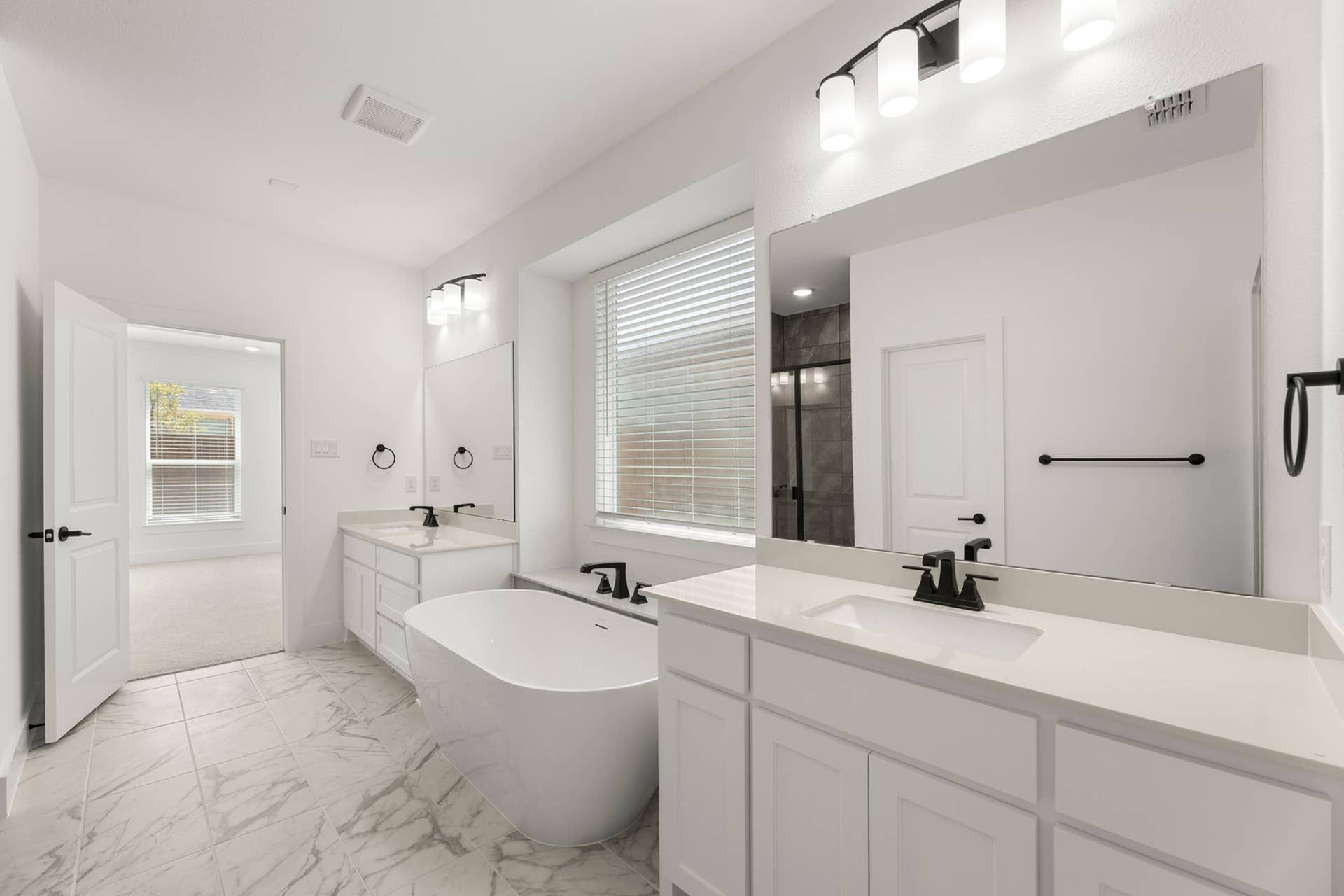 Modern bathroom with freestanding tub, dual sinks, and marble tile flooring.