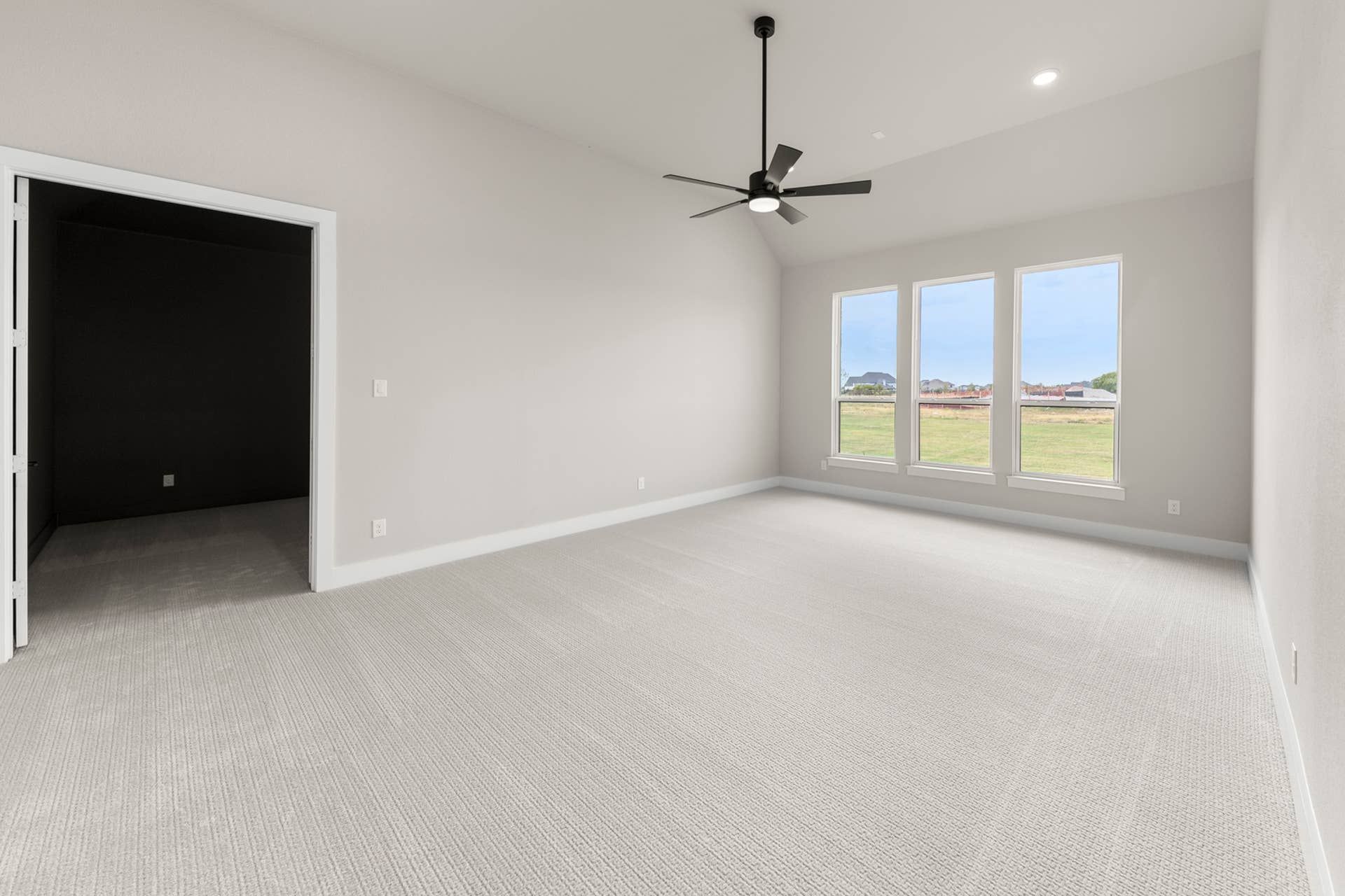 Spacious room with vaulted ceiling, large windows, and modern ceiling fan.