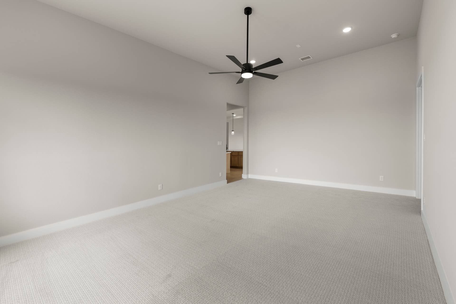 Spacious room with ceiling fan and neutral carpet flooring.