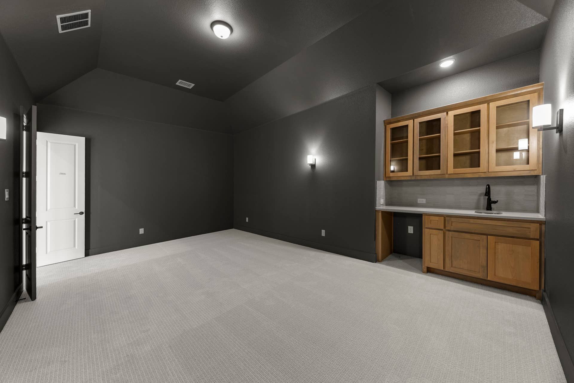 Spacious interior room with wet bar, gray walls, and white carpet.