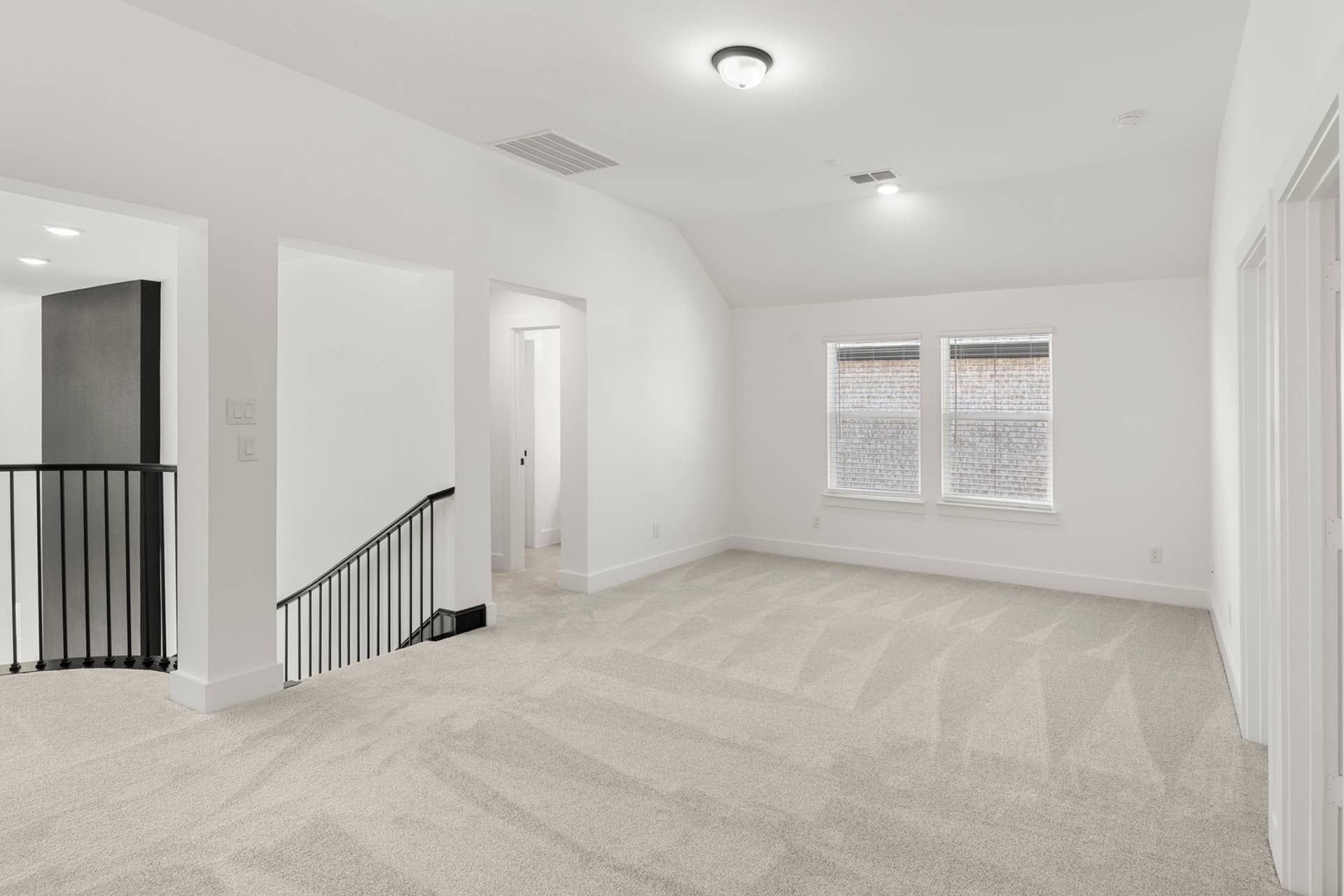 Spacious carpeted interior room with stairway and natural light from double windows.