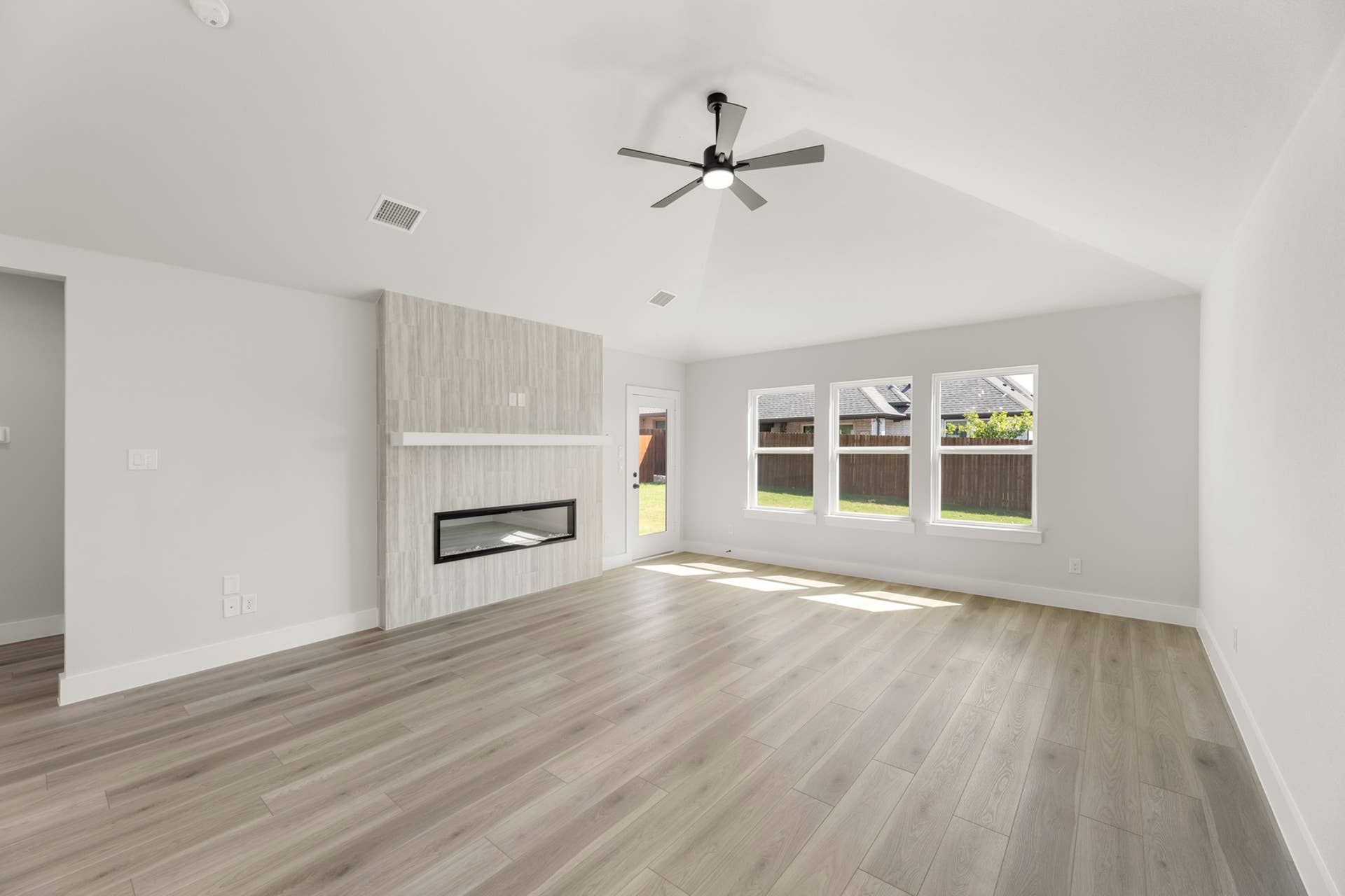 Spacious living room with modern fireplace, ceiling fan, and large windows.