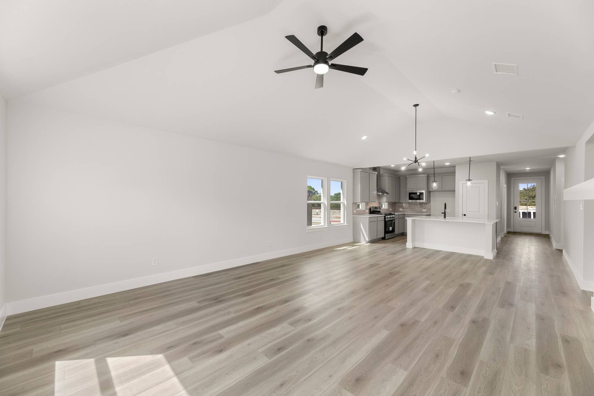 Spacious modern kitchen and living area with light wood flooring and ceiling fans.
