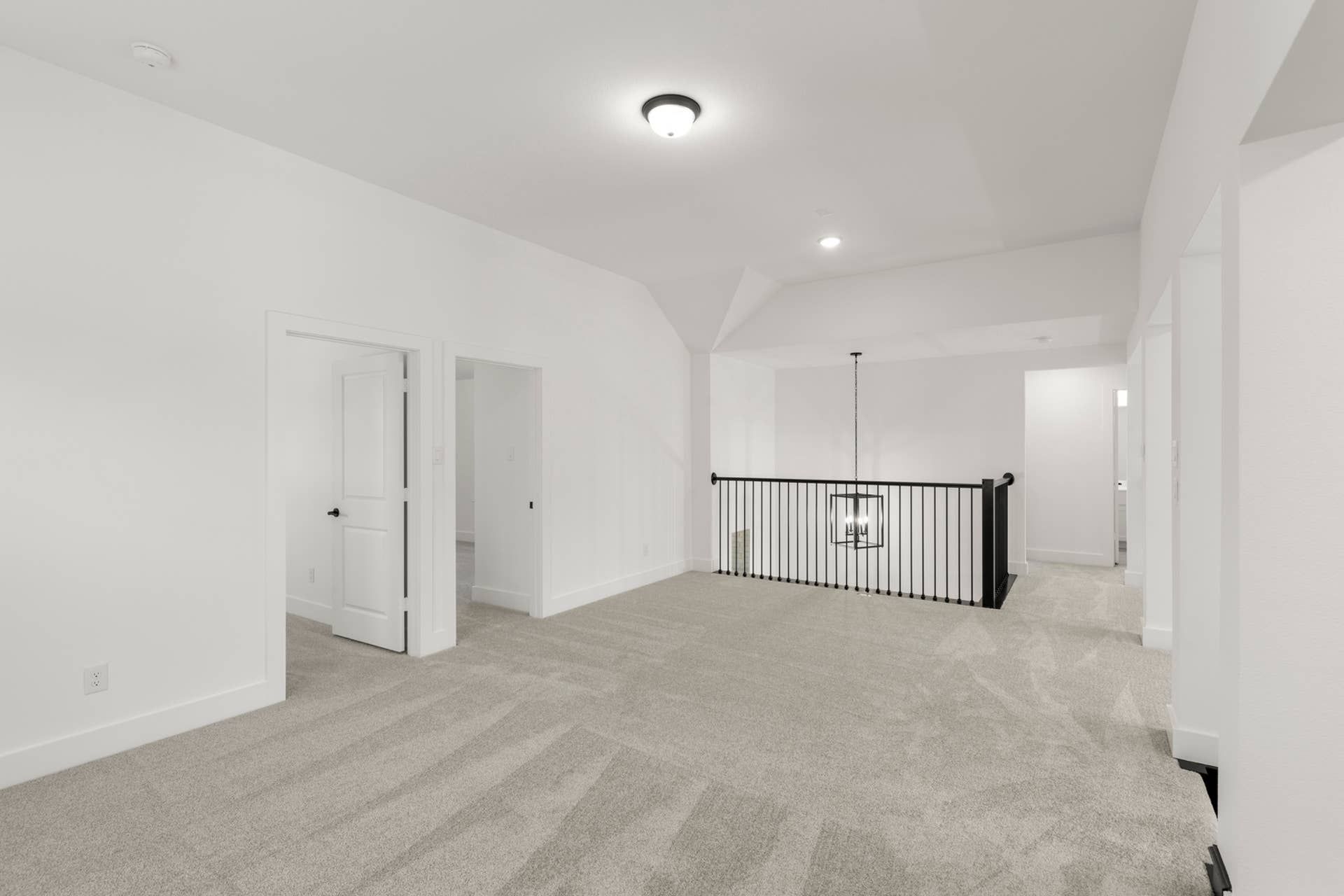 Spacious carpeted interior with modern railing and overhead lighting fixture.