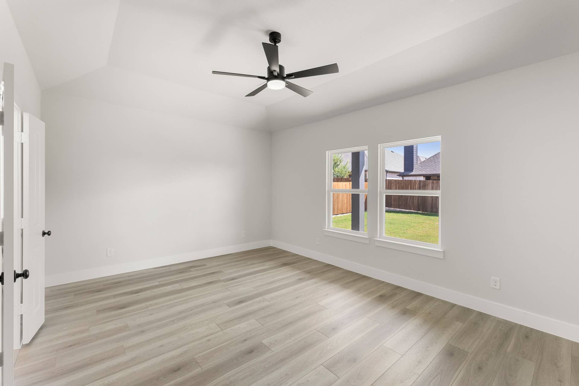 Spacious interior room with ceiling fan, wood flooring, and large windows.