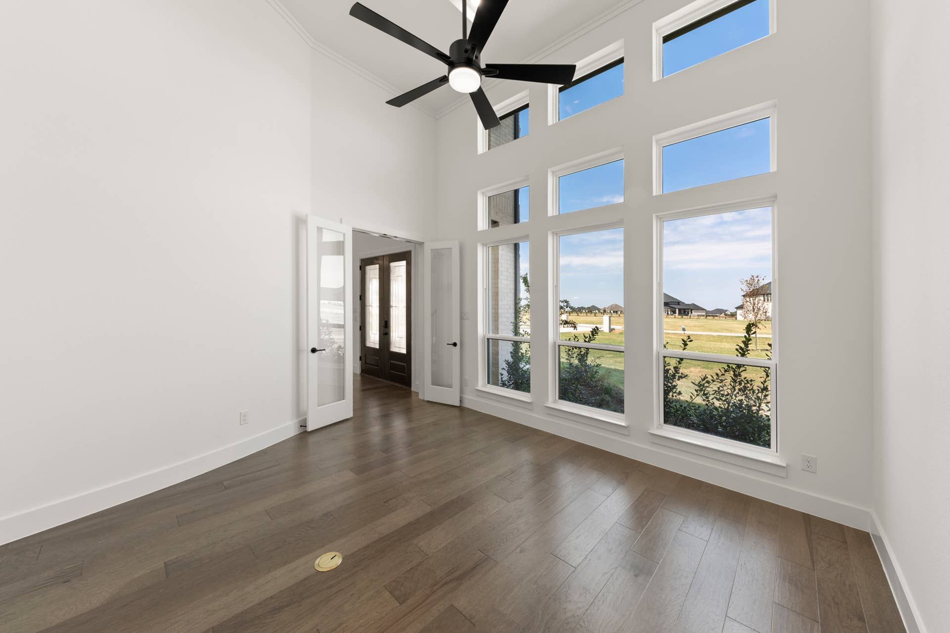 Bright study room with large windows, wood floors, and modern ceiling fan.