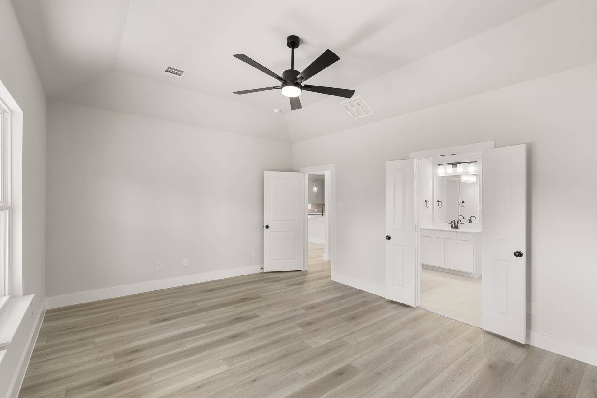 Spacious room with wood flooring and ceiling fan, leading to a bathroom.