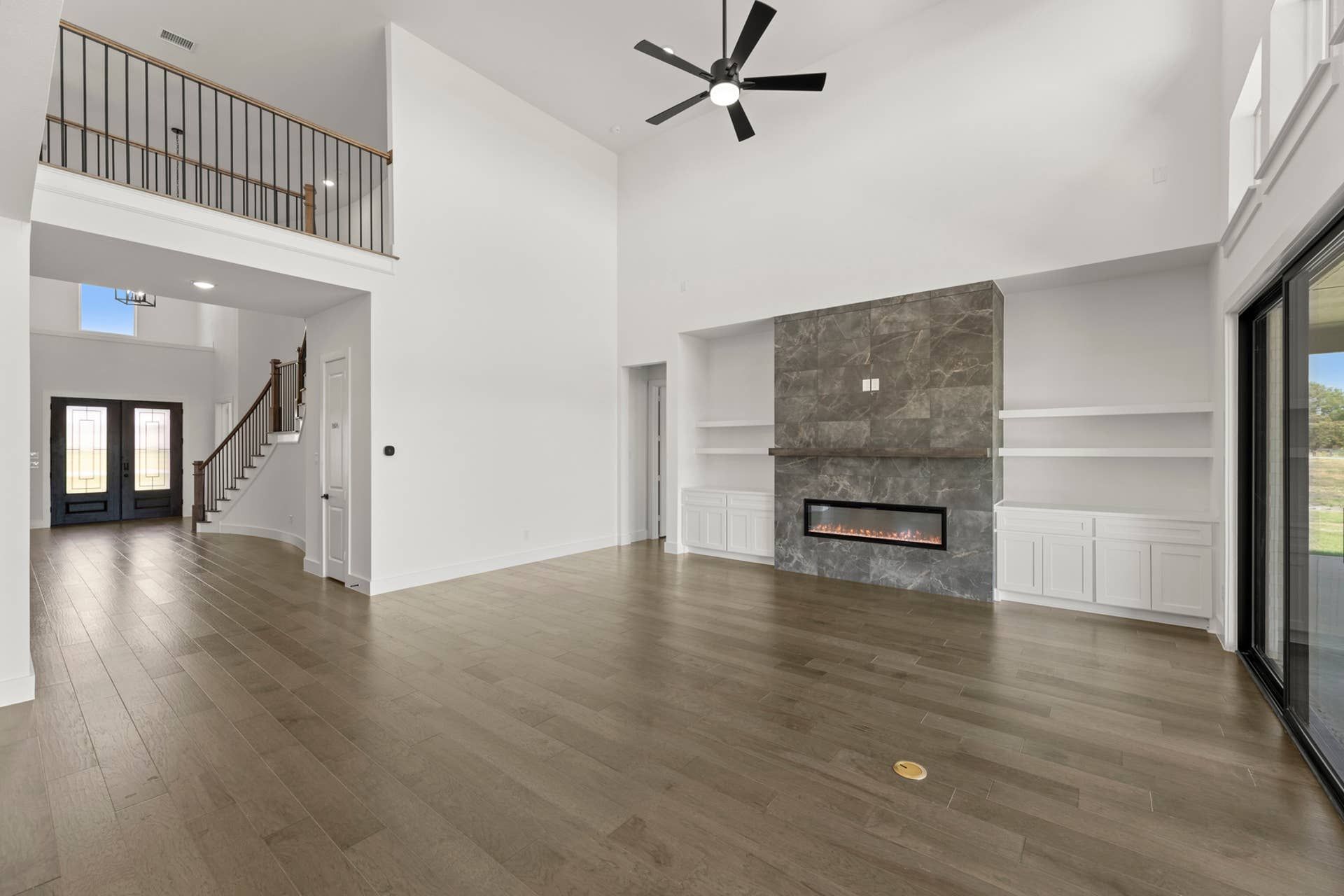 Spacious living room with high ceiling, modern fireplace, and elegant staircase.