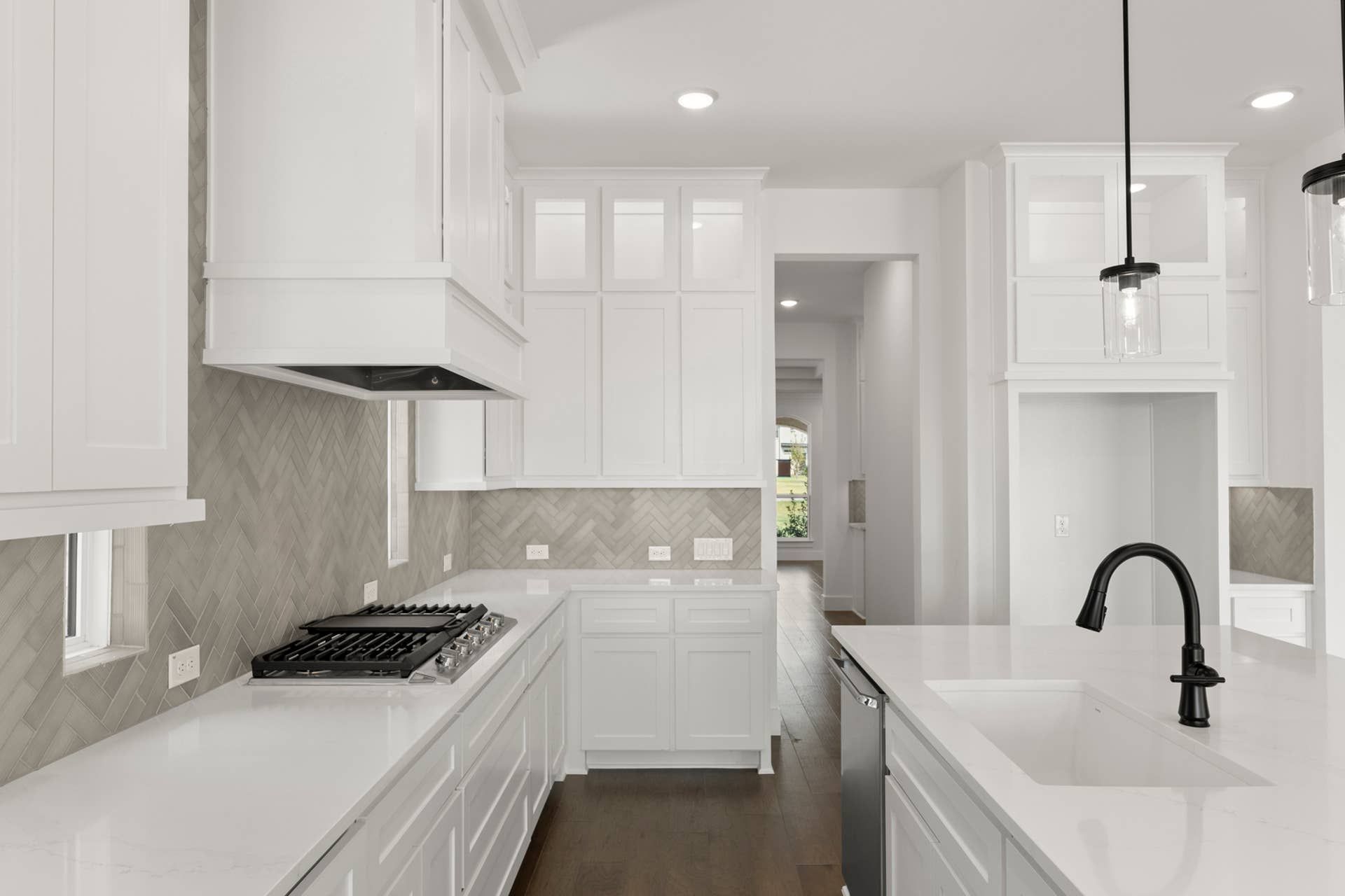 Modern kitchen with white cabinetry, herringbone backsplash, and island sink.