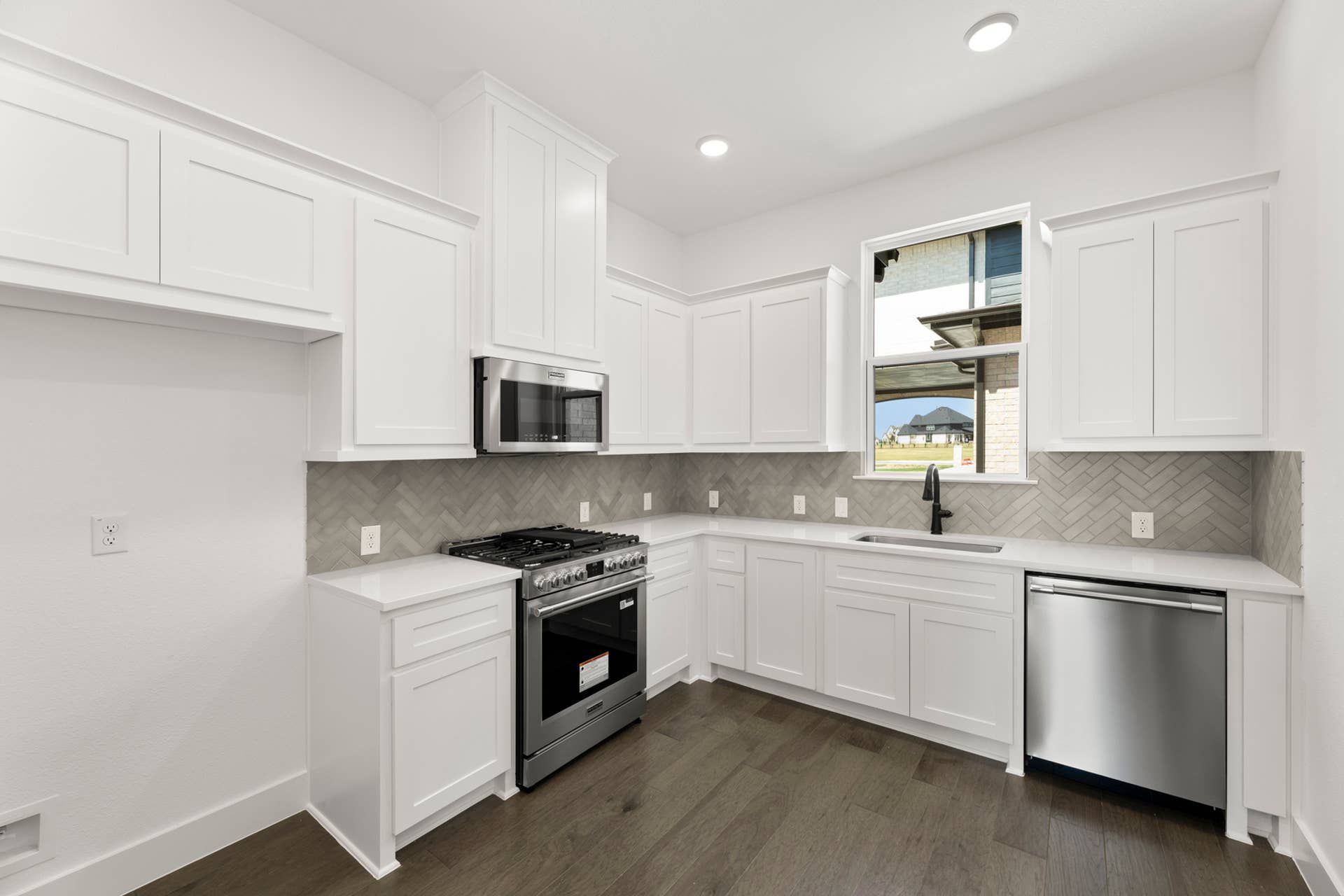 Modern kitchen with white cabinetry, stainless steel appliances, and herringbone backsplash.