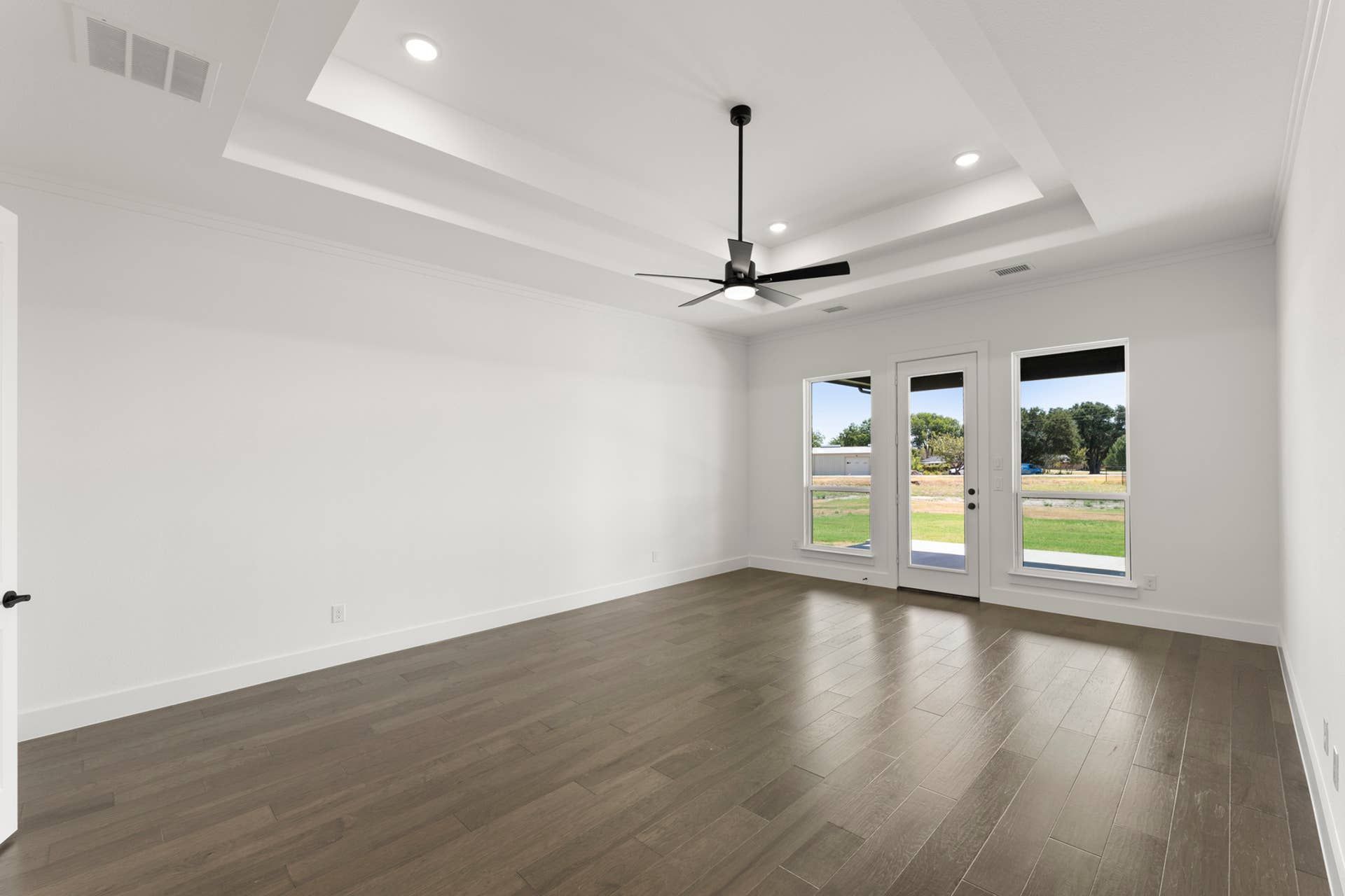 Spacious room with tray ceiling, ceiling fan, and large windows overlooking greenery.