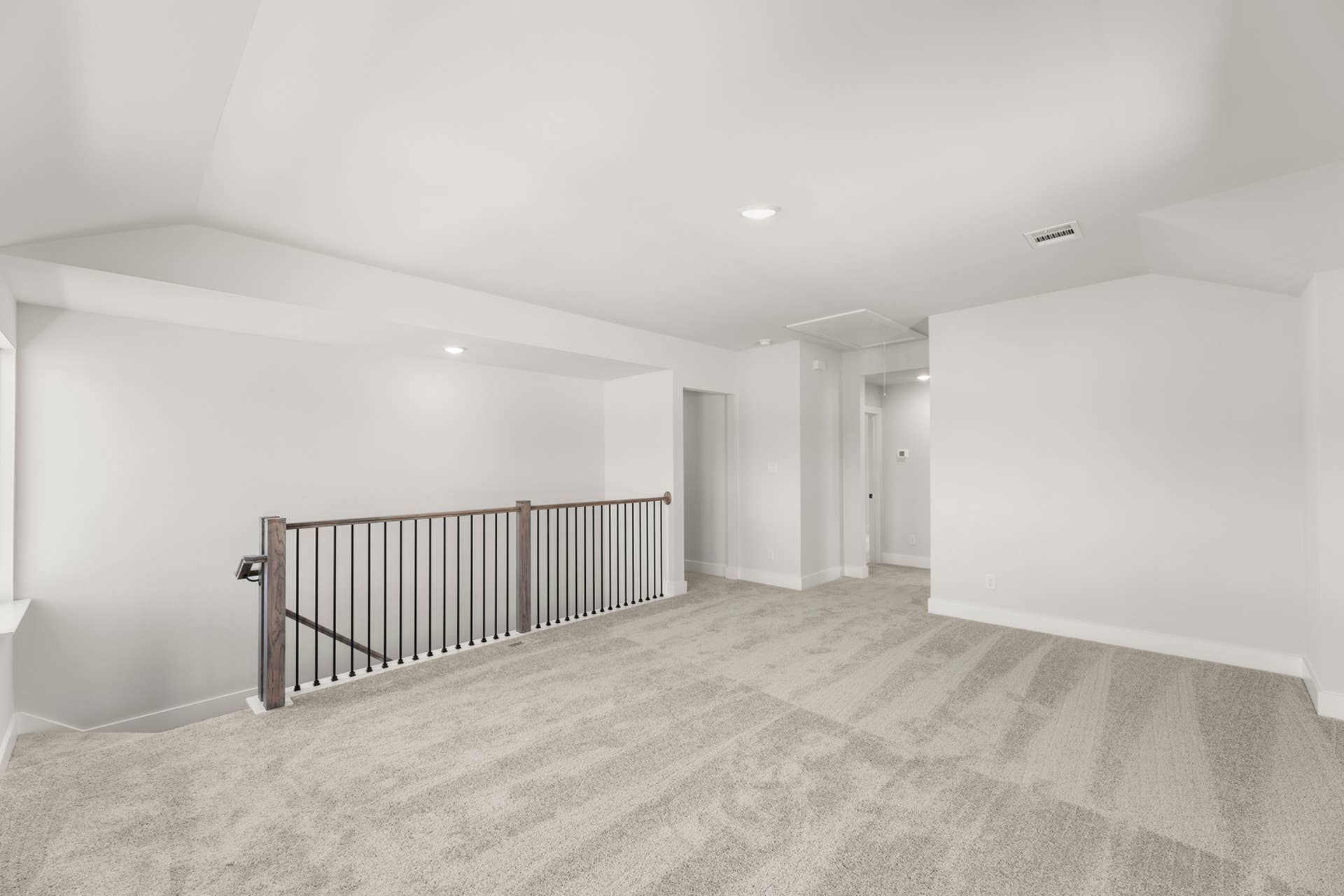 Spacious carpeted loft area with railing and recessed lighting.