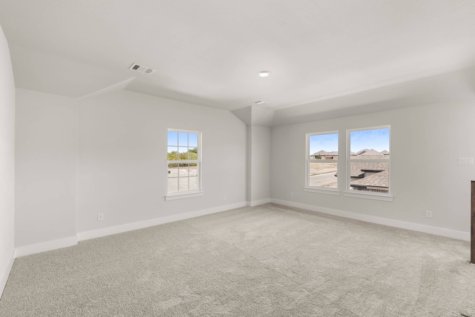 Spacious carpeted room with three windows offering natural light and neighborhood view.