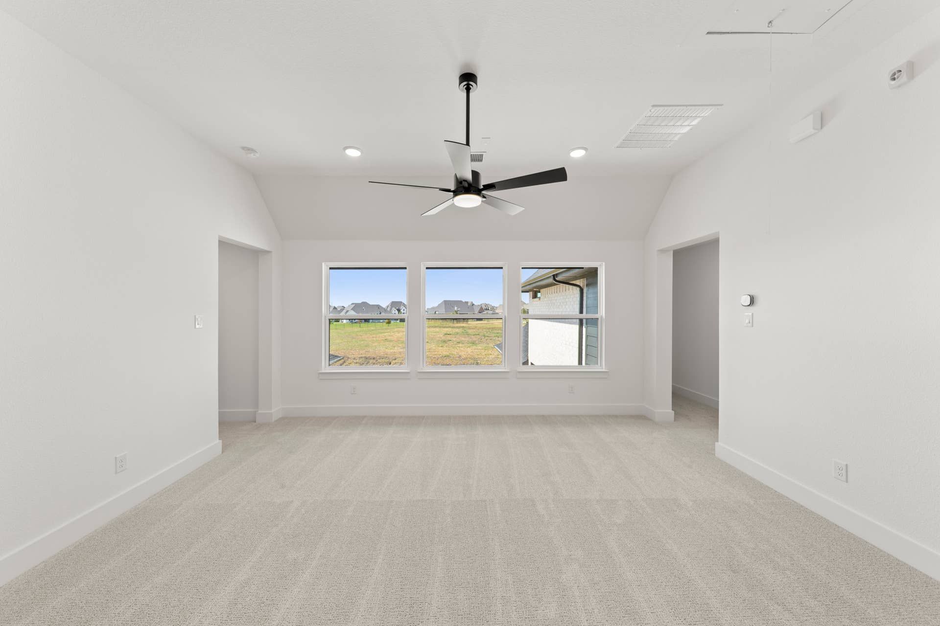 Spacious interior with ceiling fan and large windows overlooking grassy landscape.