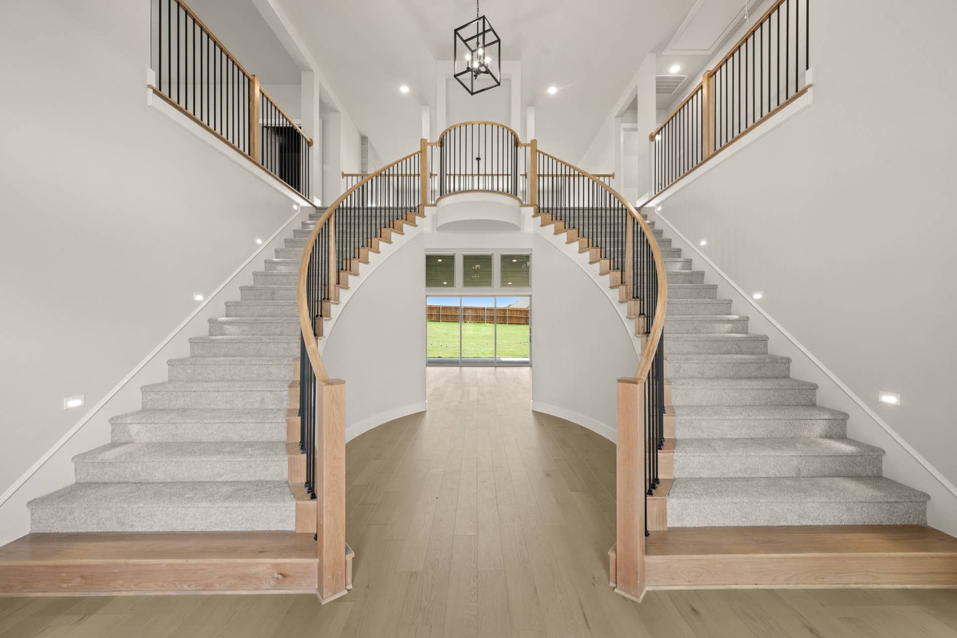 Grand entryway with dual curved staircases and modern chandelier.