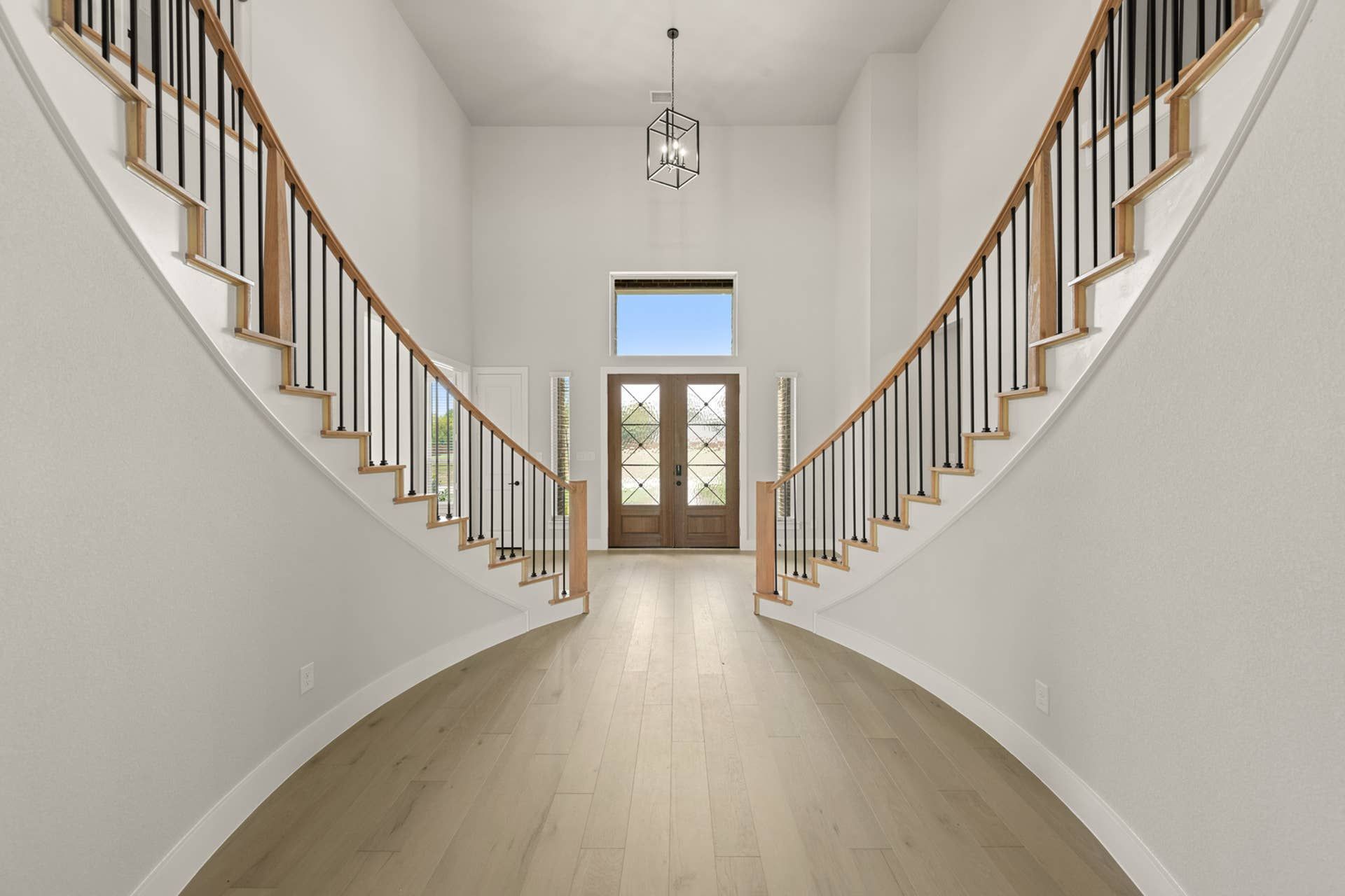 Elegant curved staircase entry with wooden doors and modern chandelier.
