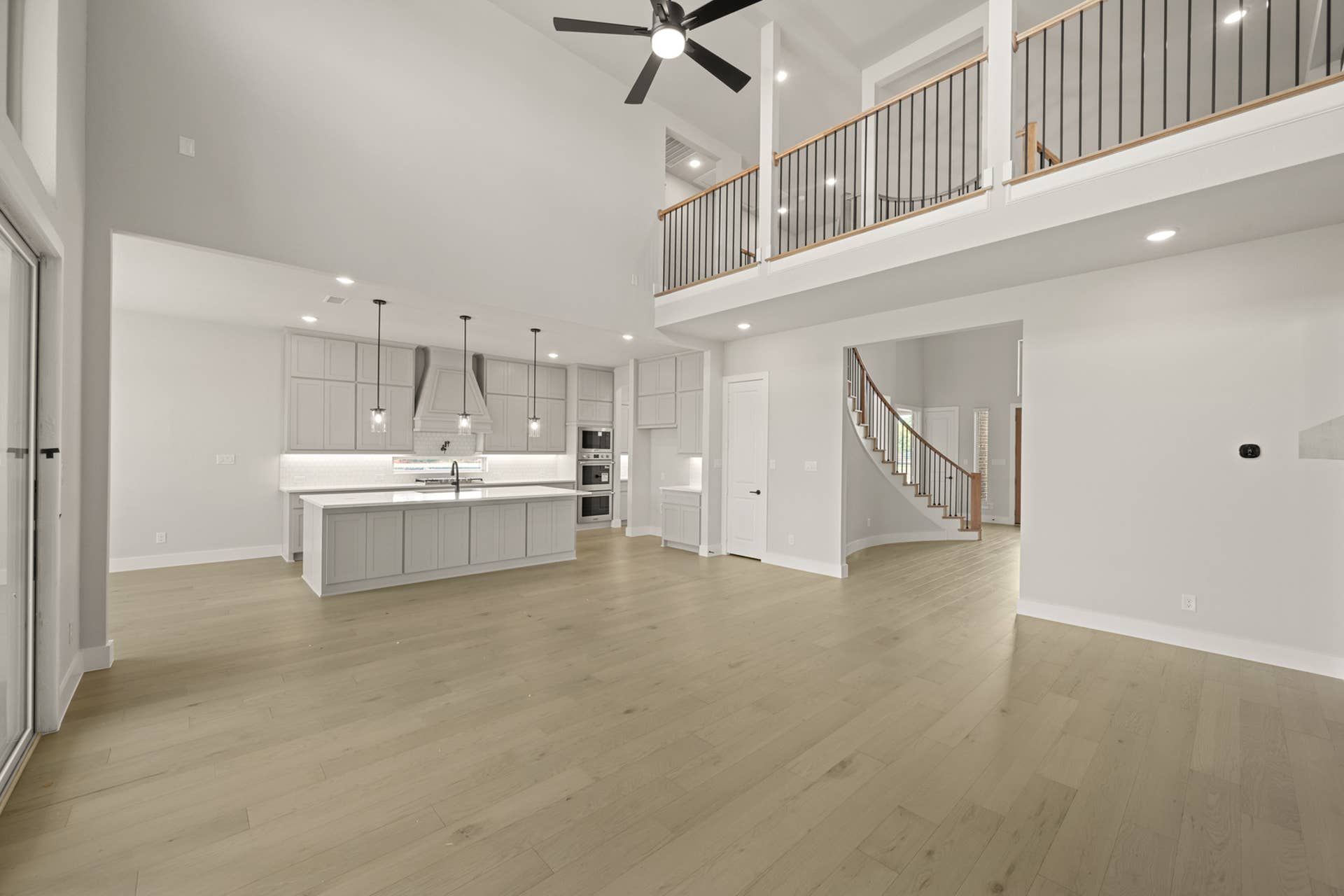 Spacious living area with vaulted ceiling, open kitchen, and curved staircase.