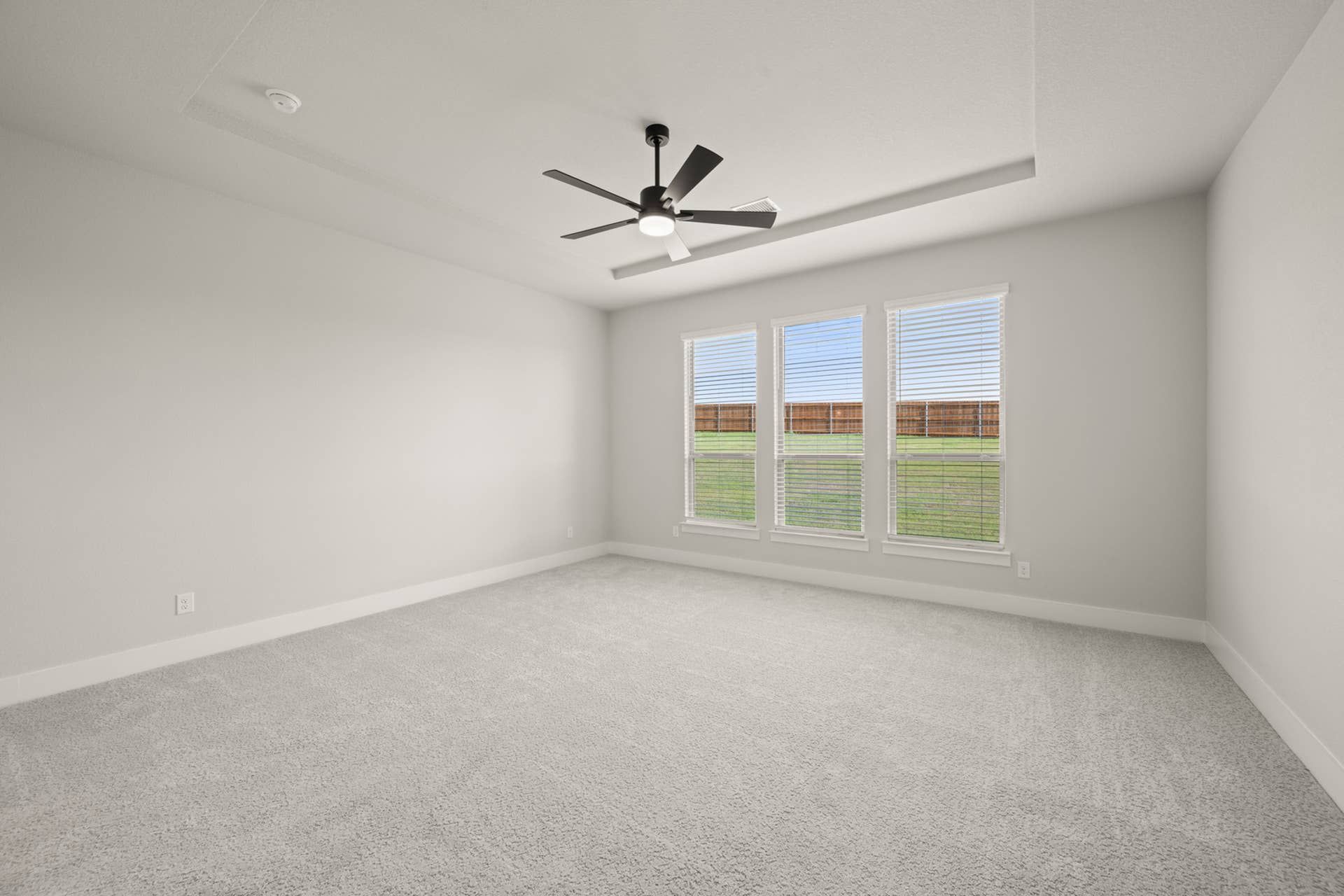 Spacious primary suite with ceiling fan and large windows overlooking backyard.