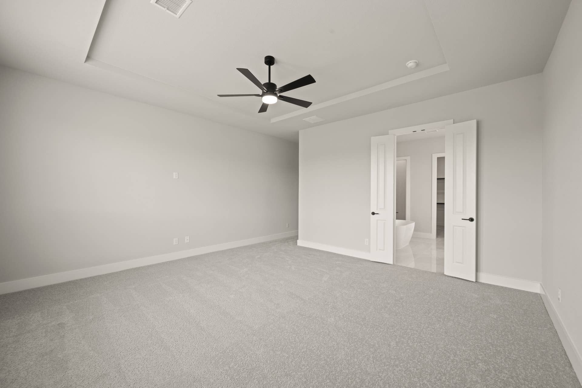 Spacious primary suite with tray ceiling and modern ceiling fan.